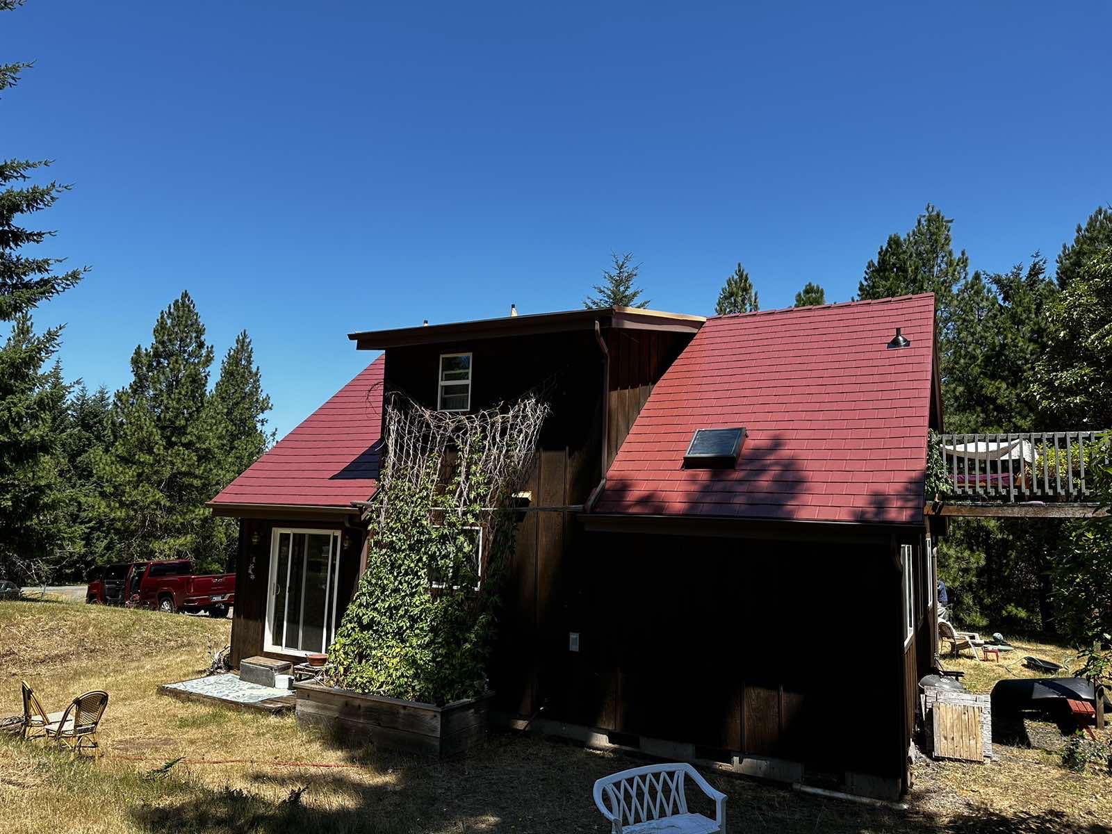 Two-story chalet-style home in Eugene, OR with steep Tile Red Interlock aluminum slate roof, dormer, and skylight surrounded by tall evergreens.