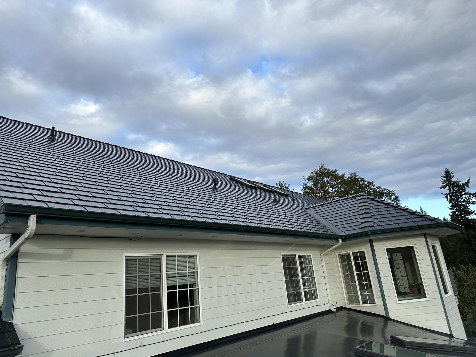 Black Interlock aluminum slate metal roof on a single-story white colonial home showing rear elevation with hip valleys, gutters, and smart vents.