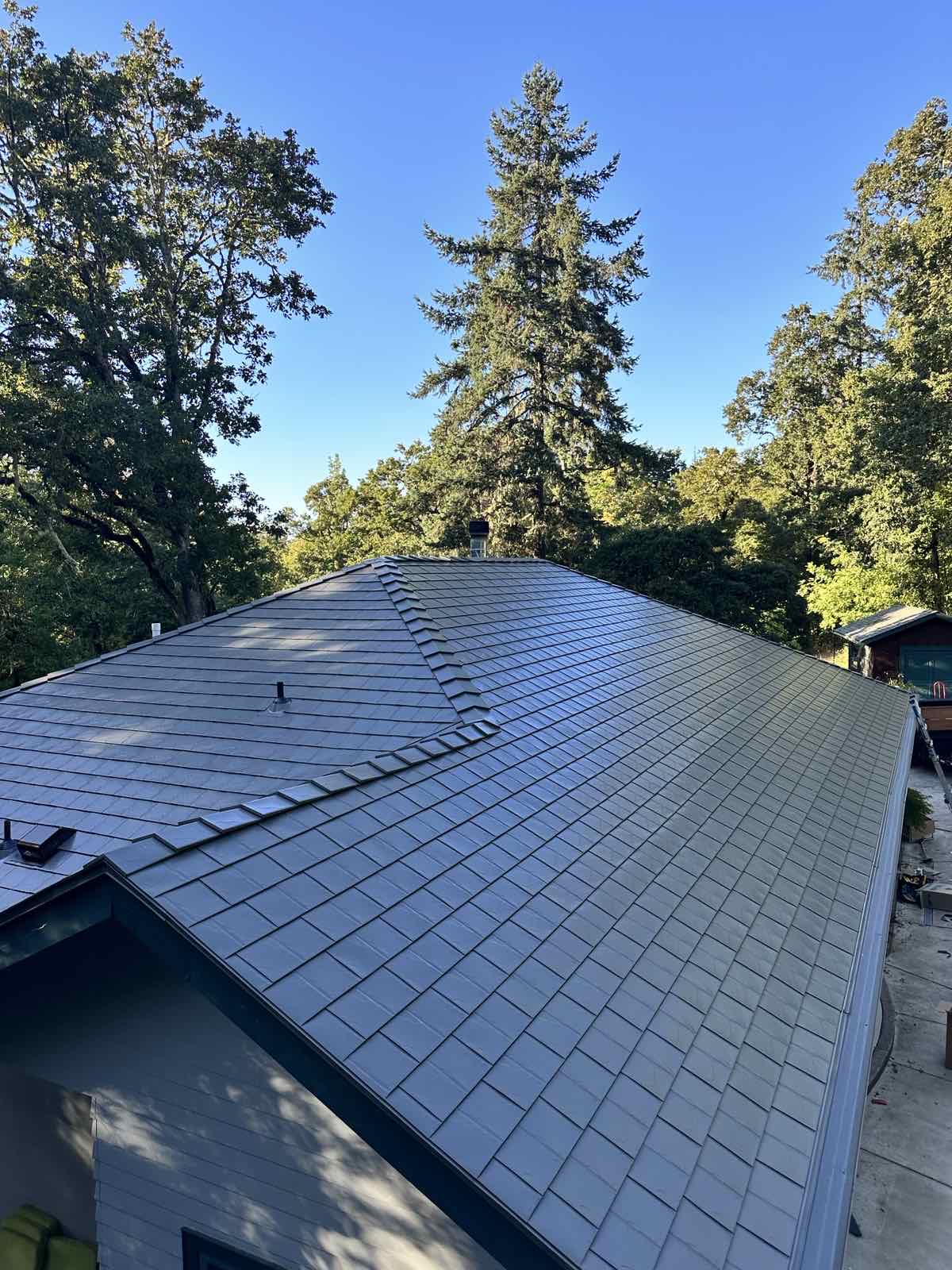 Aerial overview of a complex multi-hip Interlock aluminum slate roof in Musket Grey on a forested single-family home in Eugene, OR.
