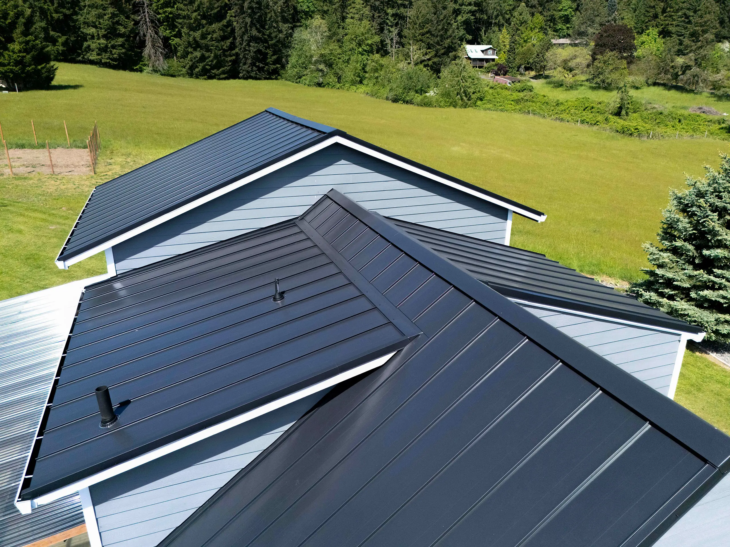 Aerial view of a black standing seam aluminum metal roof with multiple gable intersections and valley details on a rural farmhouse in Warren, OR.