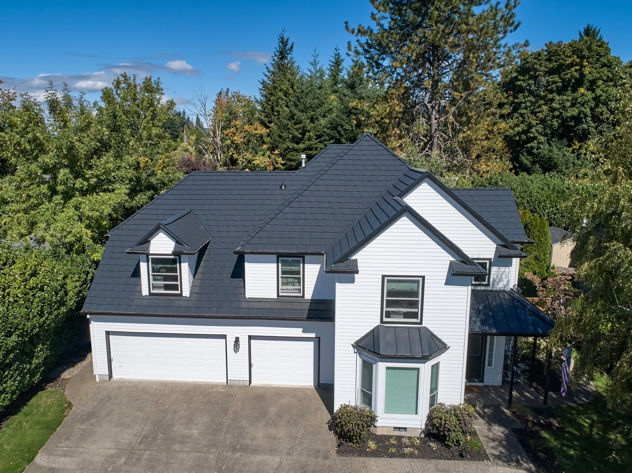 Deep Charcoal Interlock Shake aluminum roof on a white two-storey home with dormers among tall evergreen, Portland, Oregon