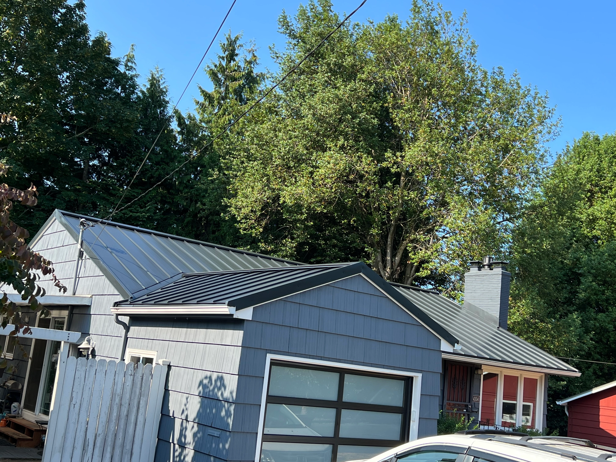 Black Interlock Standing Seam aluminum roof on a grey home with a metal roof among tall trees, Portland, Oregon