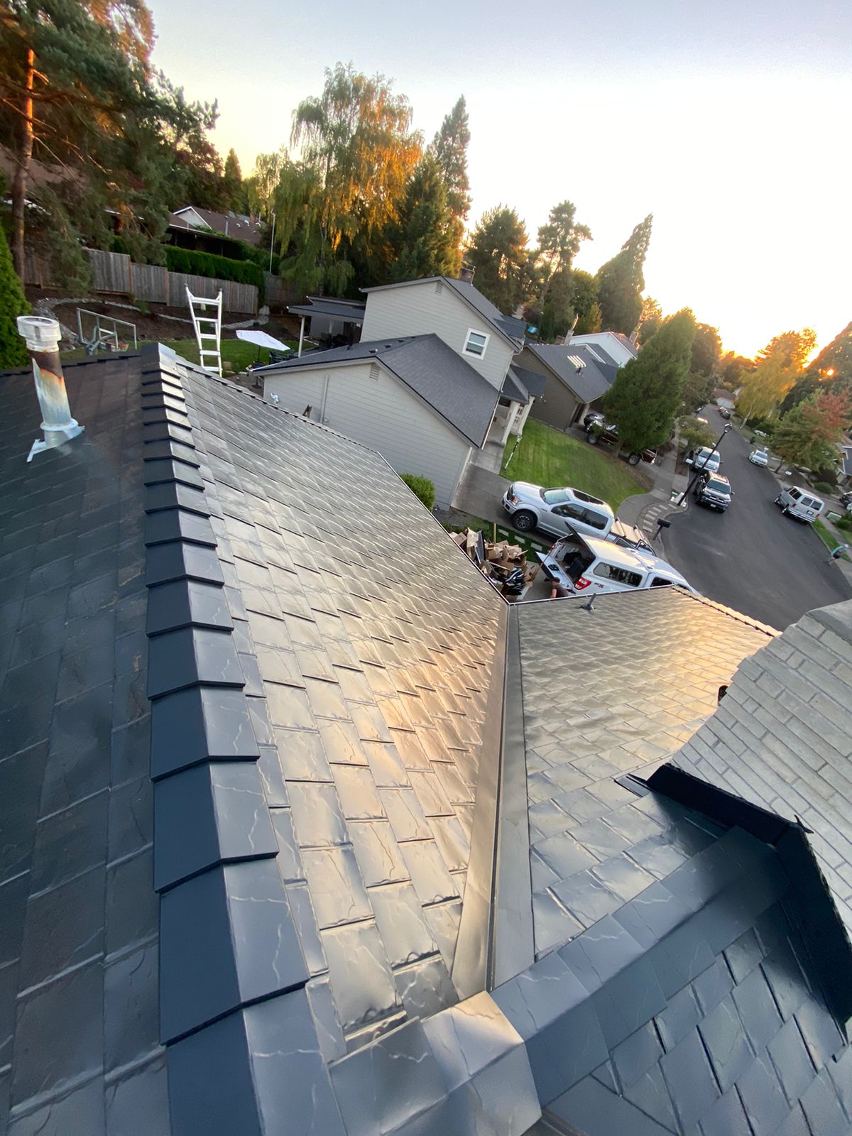Aerial view of a complex black Interlock aluminum slate metal roof with multiple valleys and ridge caps on a suburban Portland home at golden hour.