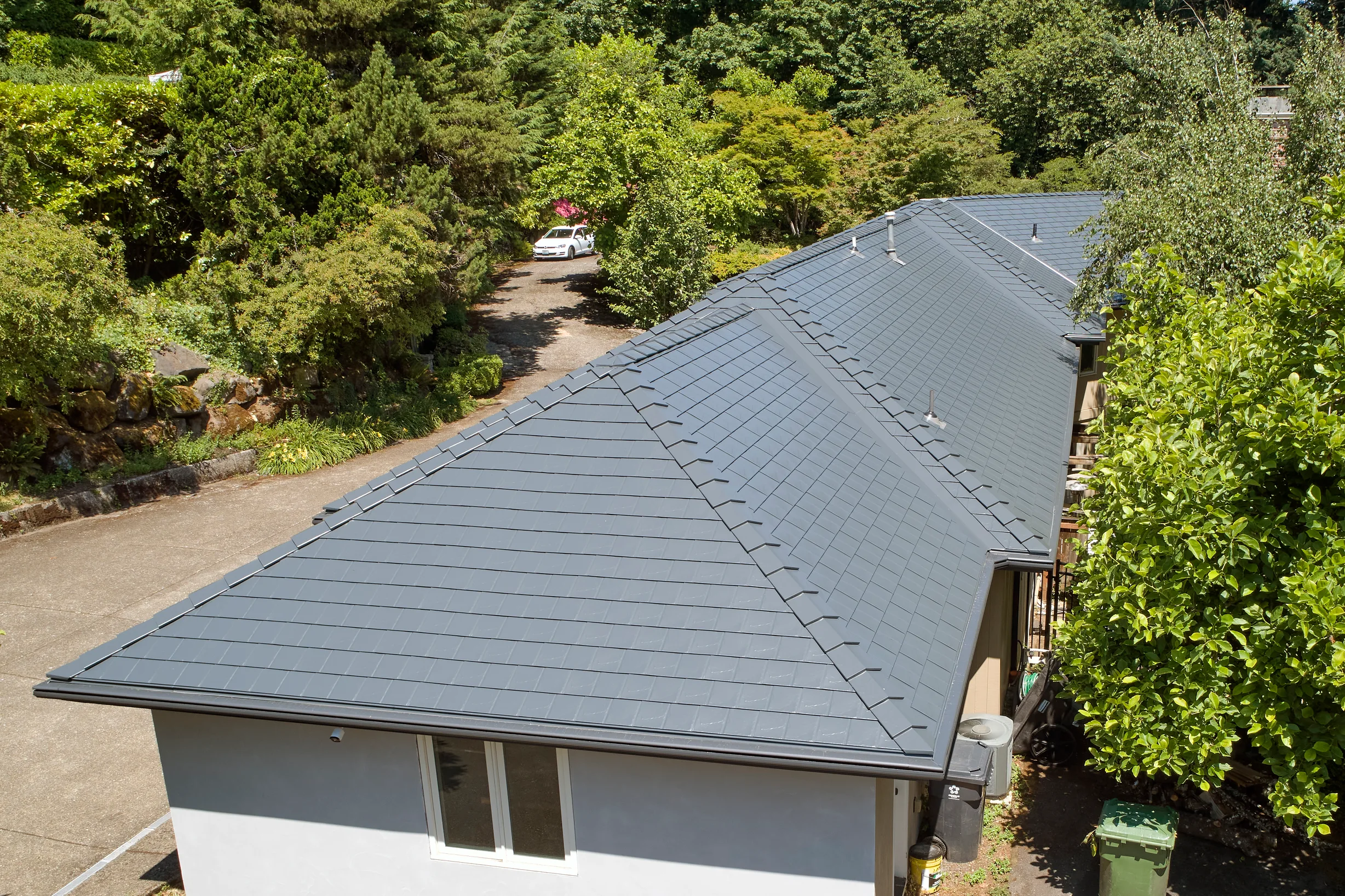 Deep Charcoal Interlock Slate aluminum roof on a white single-family home with a metal roof among trees, Portland, Oregon
