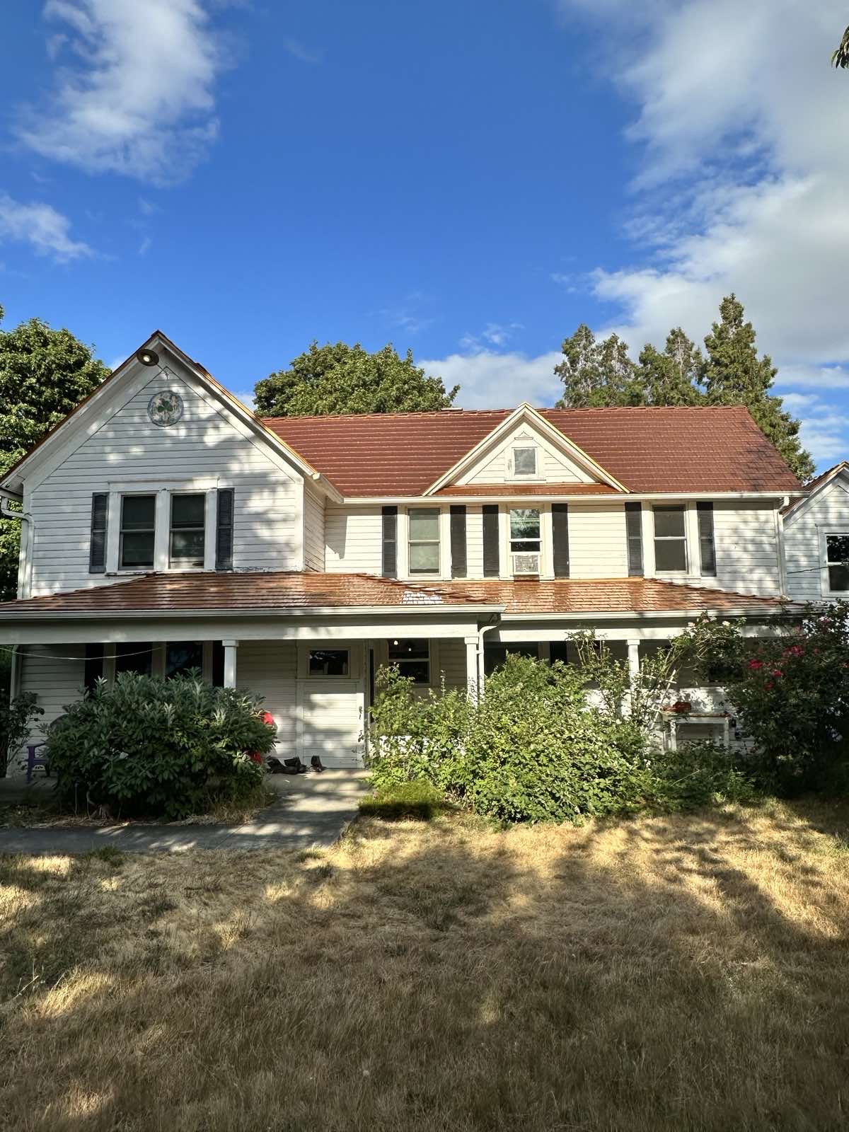 Two-story farmhouse in McMinnville, OR featuring an Interlock Copper Penny cedar shingle aluminum metal roof with dormers and a wraparound porch.