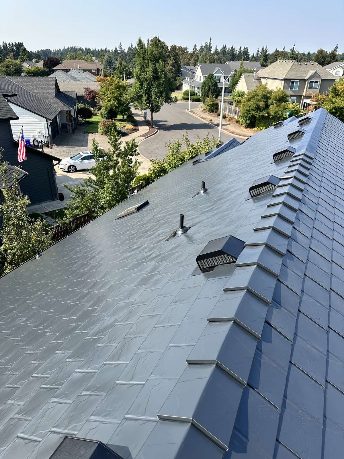 Aerial view of Interlock aluminum slate metal roofing in charcoal-black on a two-story craftsman home in Oregon City, OR, showing ridge vents and vent pipes.
