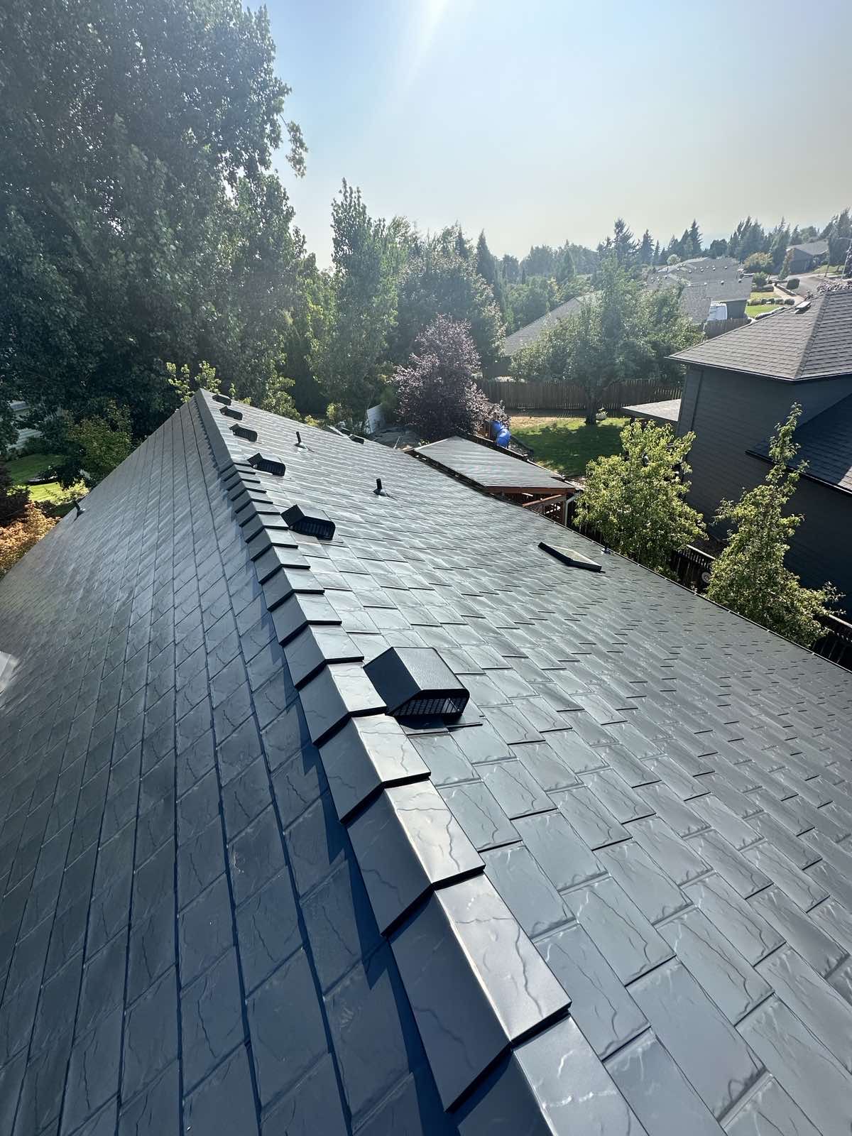 Aerial view of a steep black Interlock aluminum slate metal roof with ridge caps and roof louvers on a Craftsman-style home in Oregon City, OR.