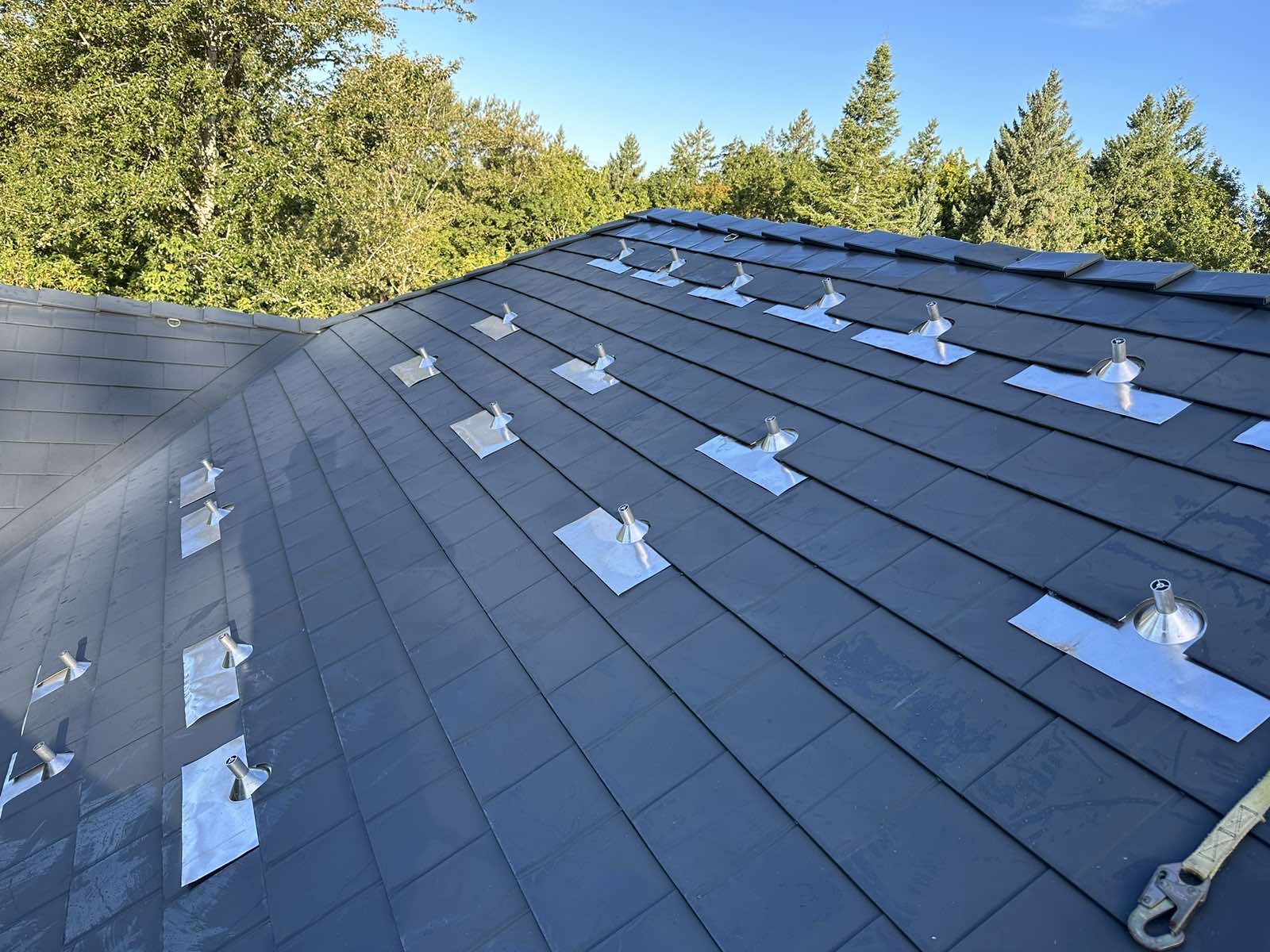 Deep charcoal Interlock aluminum slate metal roof on a hip-style home, featuring numerous silver vent pipe flashings across the field in Portland, OR.