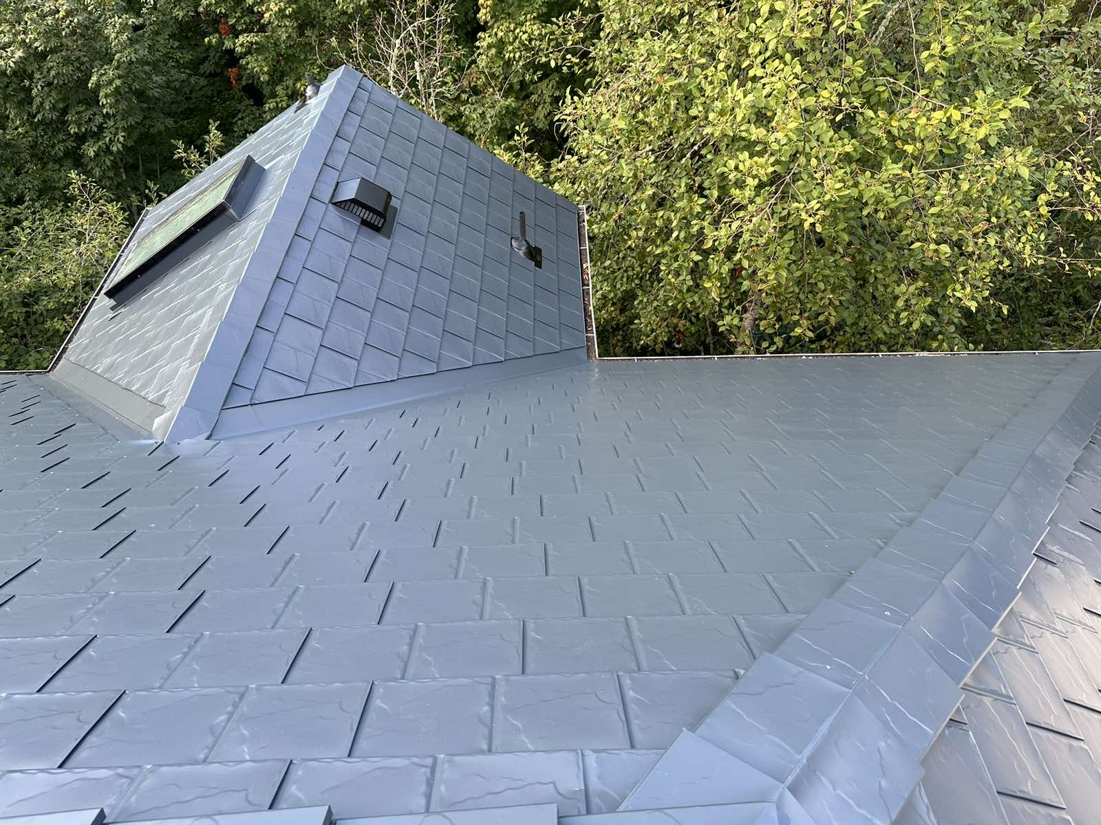 Aerial view of a complex multi-hip deep charcoal Interlock aluminum slate roof with a pyramid dormer, valleys, and vents, surrounded by lush green trees in Portland, OR.