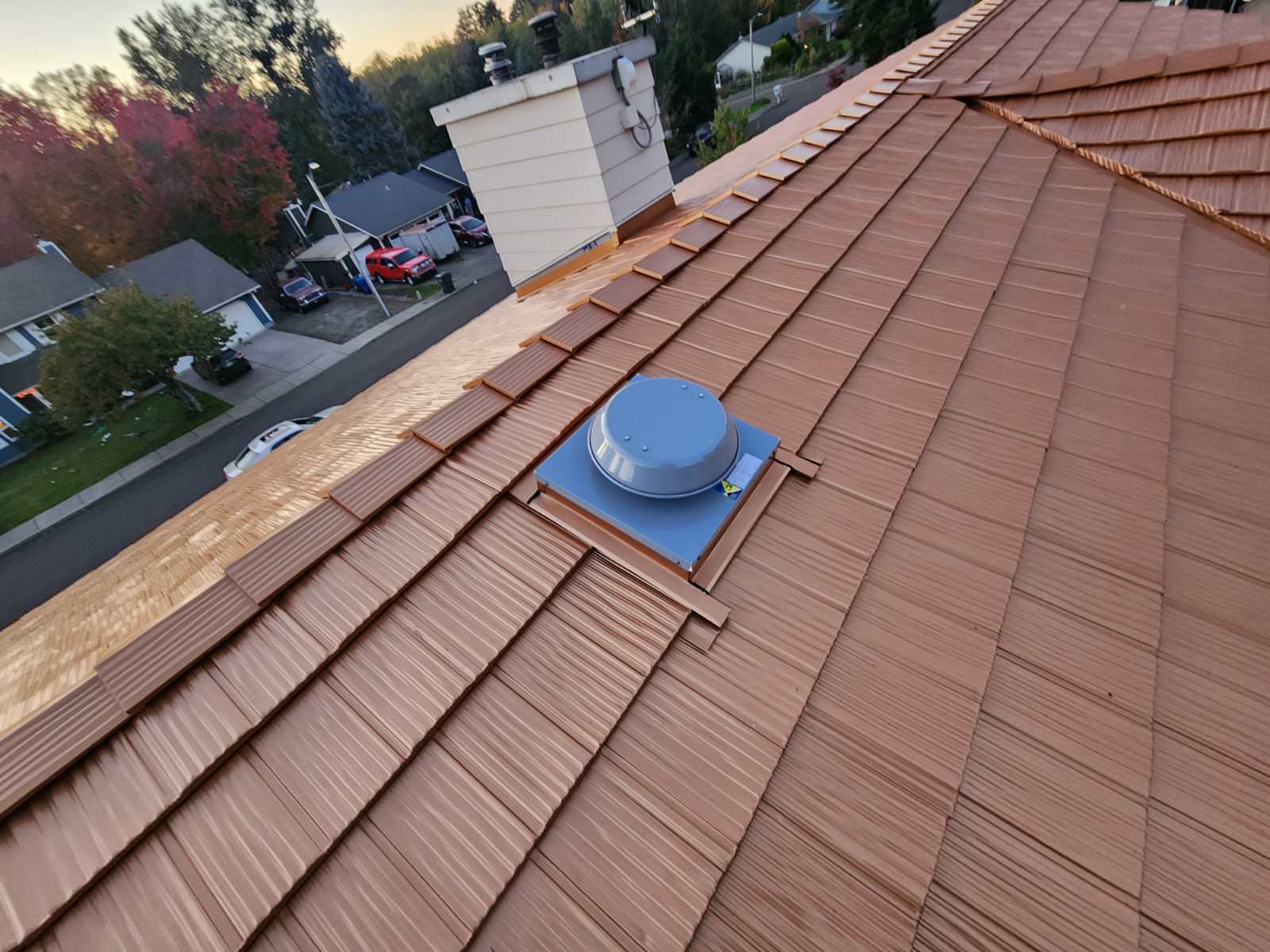Copper Penny Interlock aluminum shake metal roofing on a steep multi-hip suburban home in Salem, OR, with a roof louver vent and chimney visible.