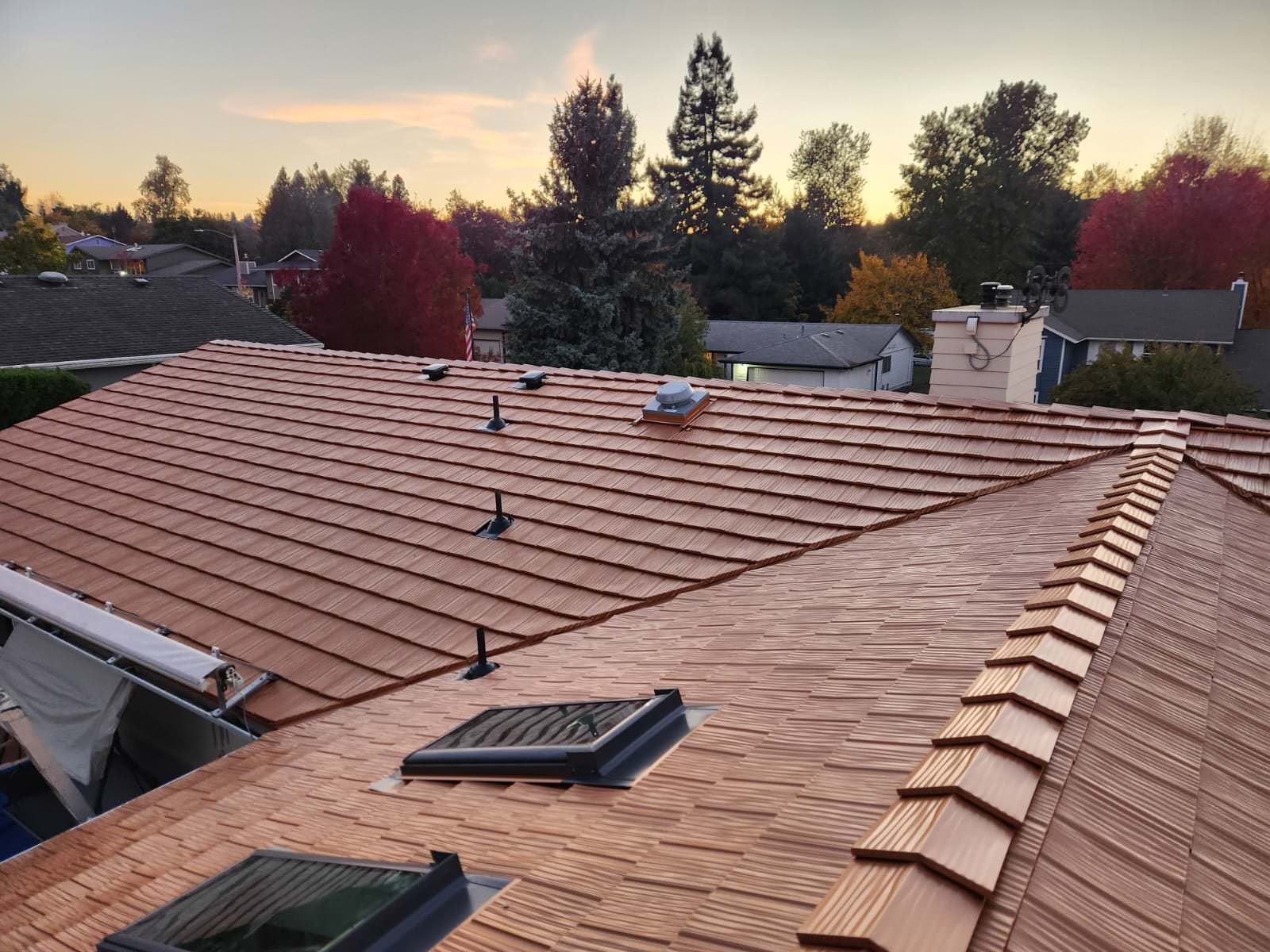 Aerial view of a complex Interlock aluminum shake roof in Copper Penny on a suburban Ranch home in Salem OR, featuring valleys, skylights, and ridge caps at golden hour.
