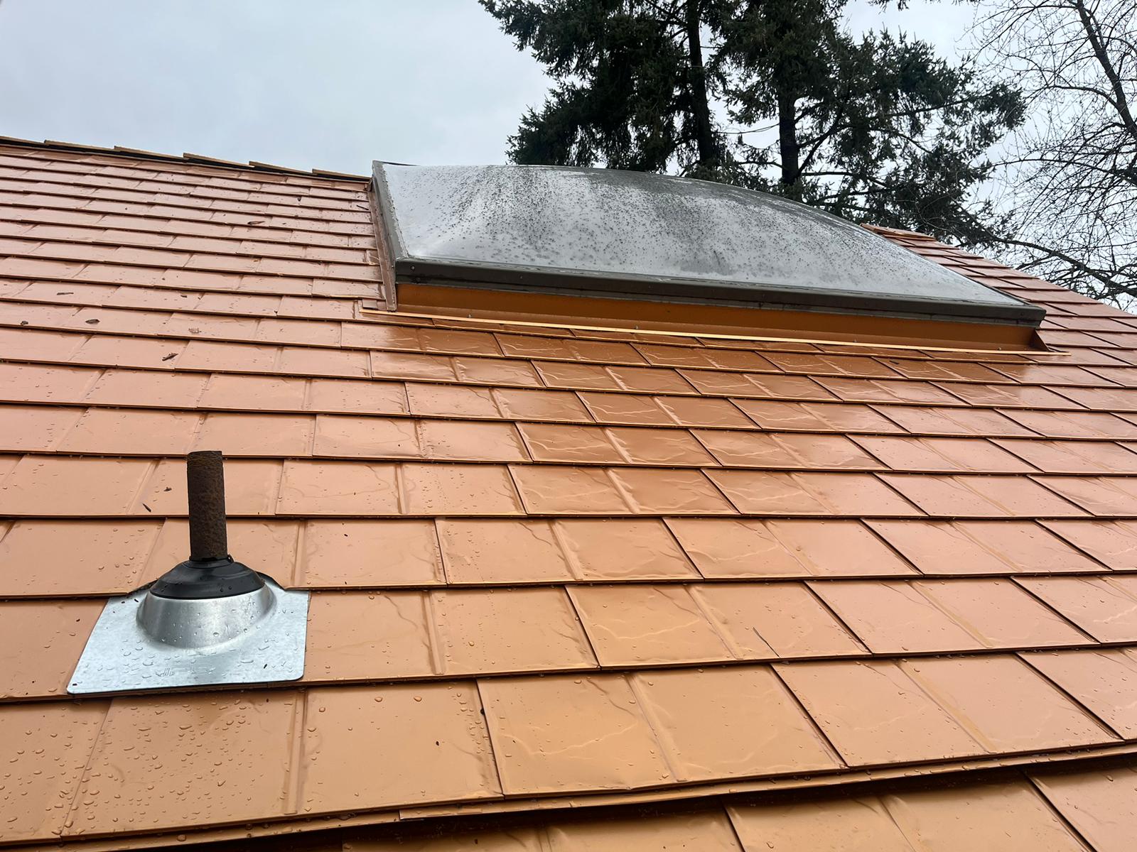 Close-up of Interlock Copper Penny aluminum slate roofing with a vent pipe boot flashing and framed skylight on a steep Portland home roof.