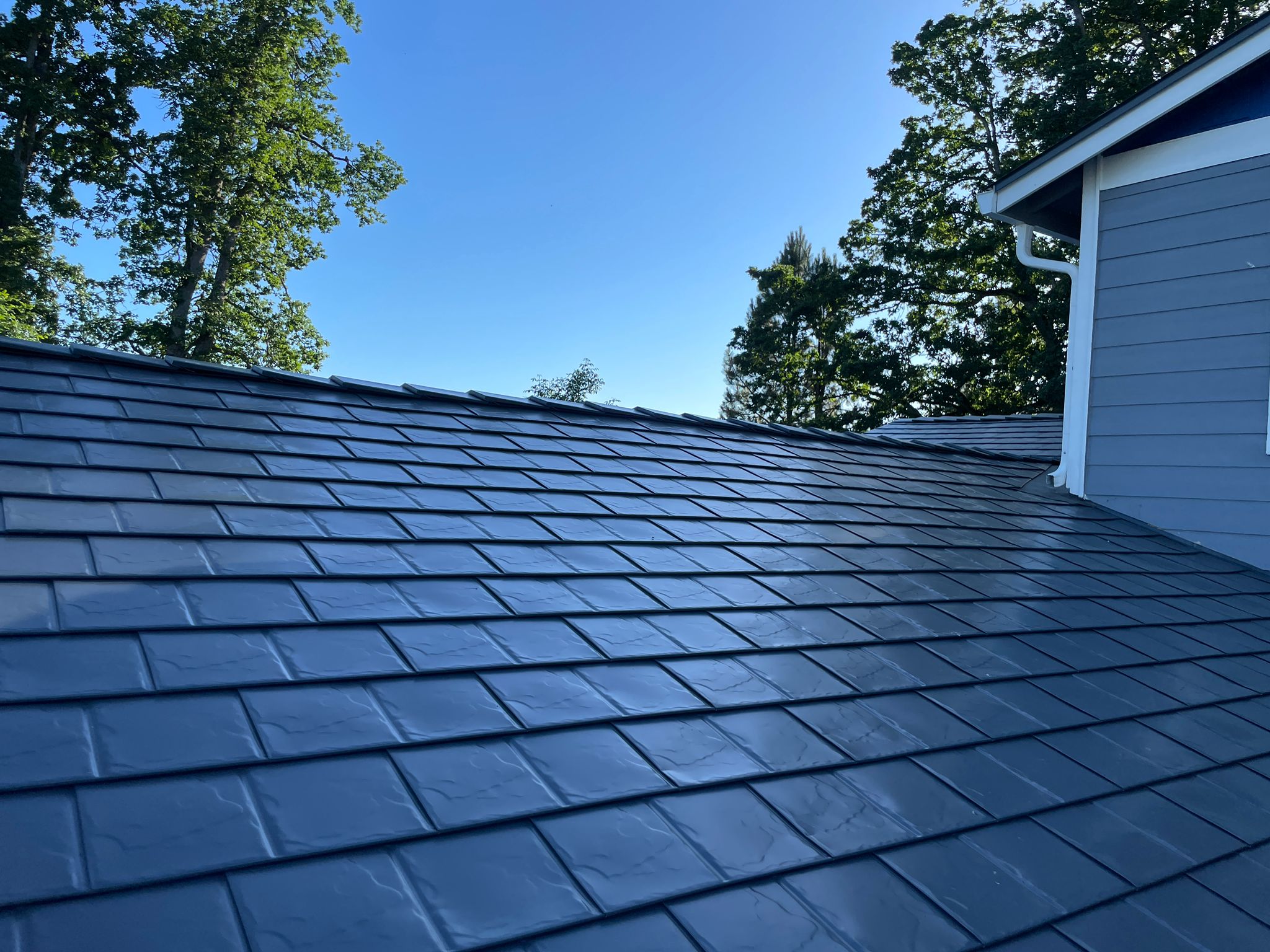 Close view of Interlock aluminum slate metal roofing in deep charcoal on a single-family home in Silverton, OR, under a clear blue sky.