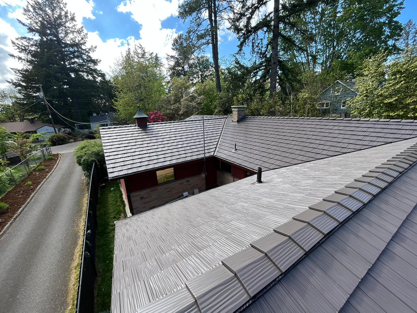 Aerial view of a complex multi-hip Interlock aluminum shake roof in Tudor Brown on a Craftsman-style home surrounded by mature trees in Portland, OR.