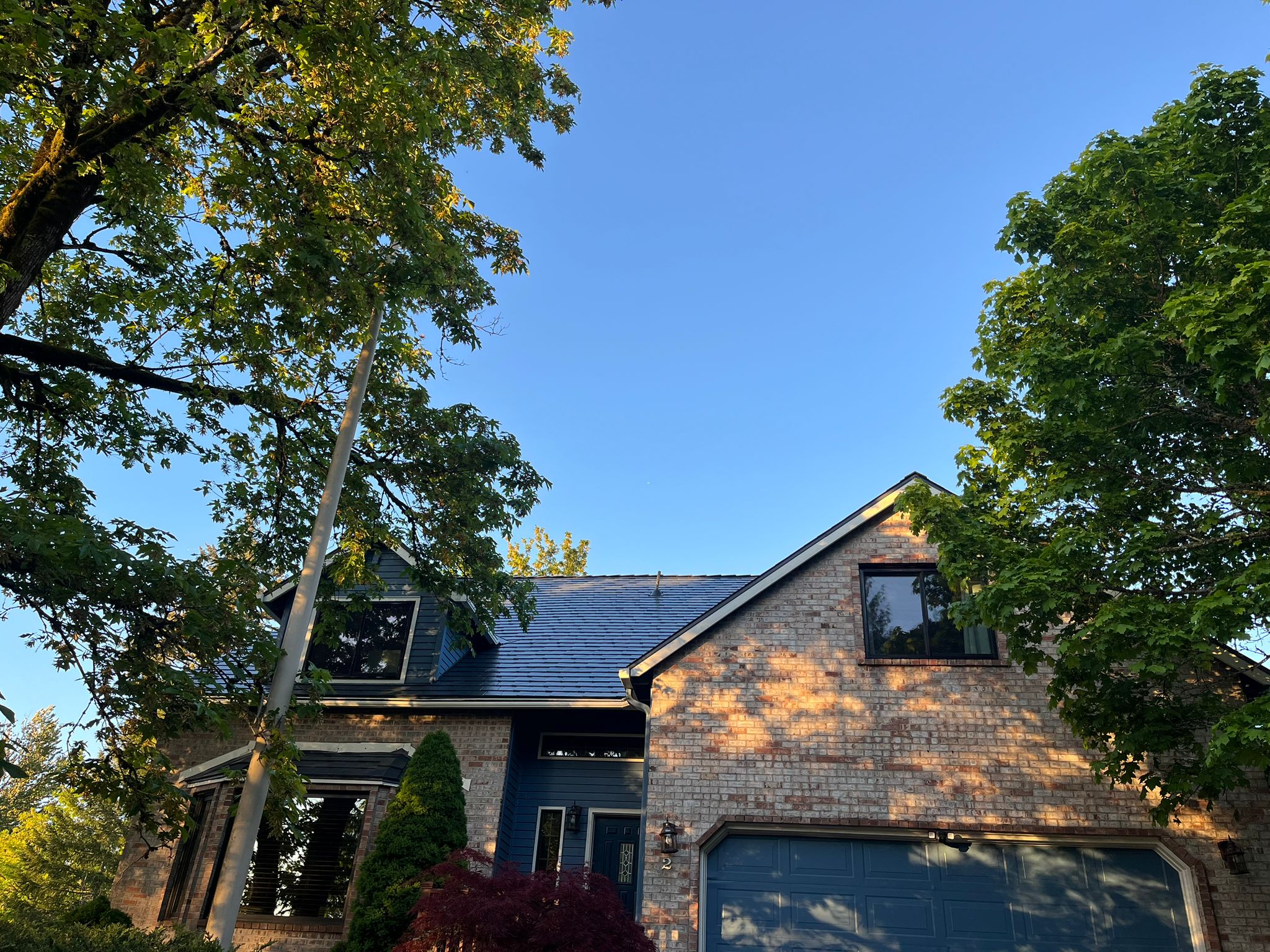 Two-story brick Craftsman home in Lake Oswego with a deep charcoal Interlock aluminum slate metal roof, dormers, and blue garage door.