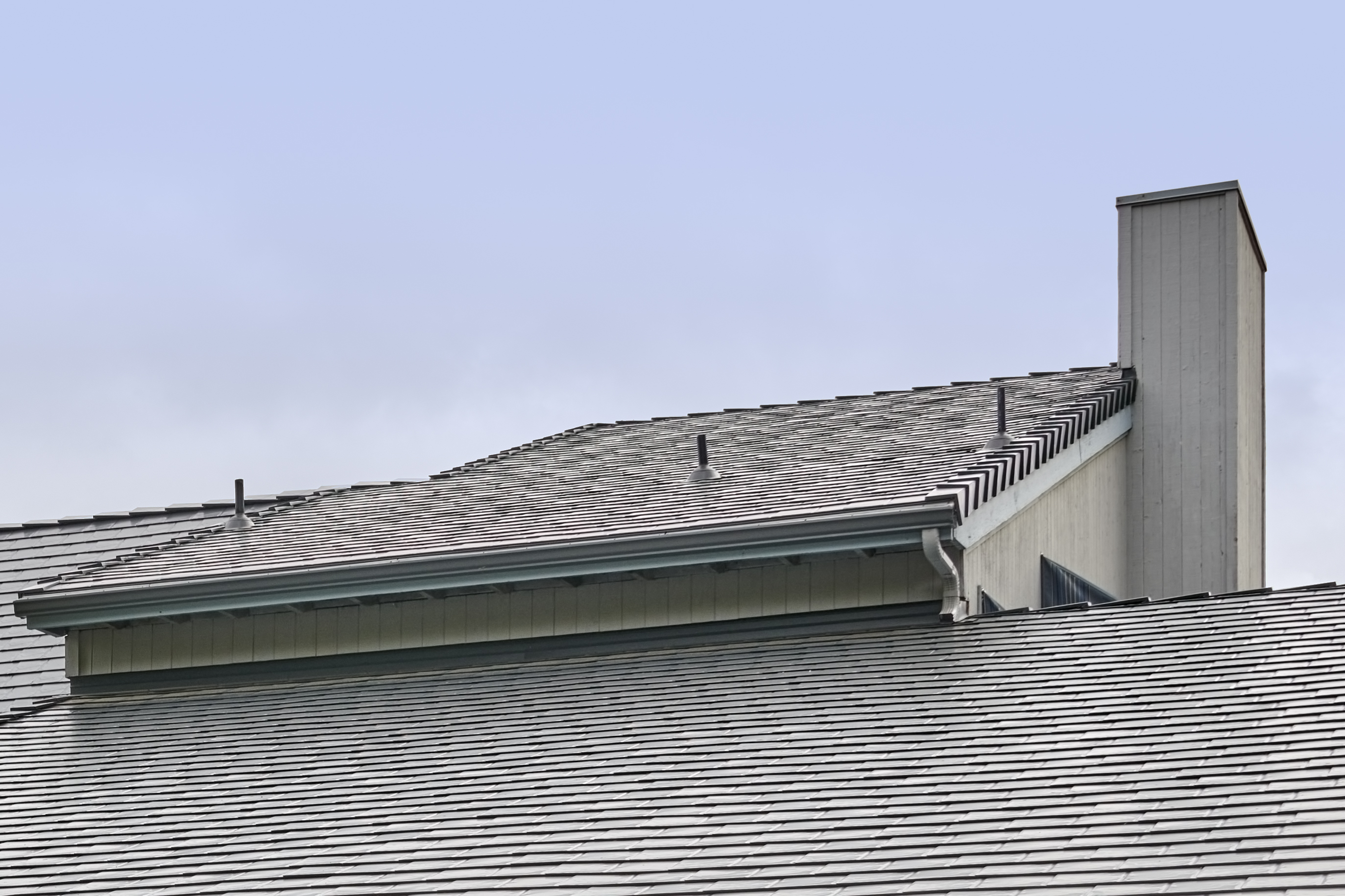 Deep charcoal Interlock aluminum slate metal roofing on a multi-level home in Amity, OR, featuring a tall chimney, vent pipes, and ridge caps.