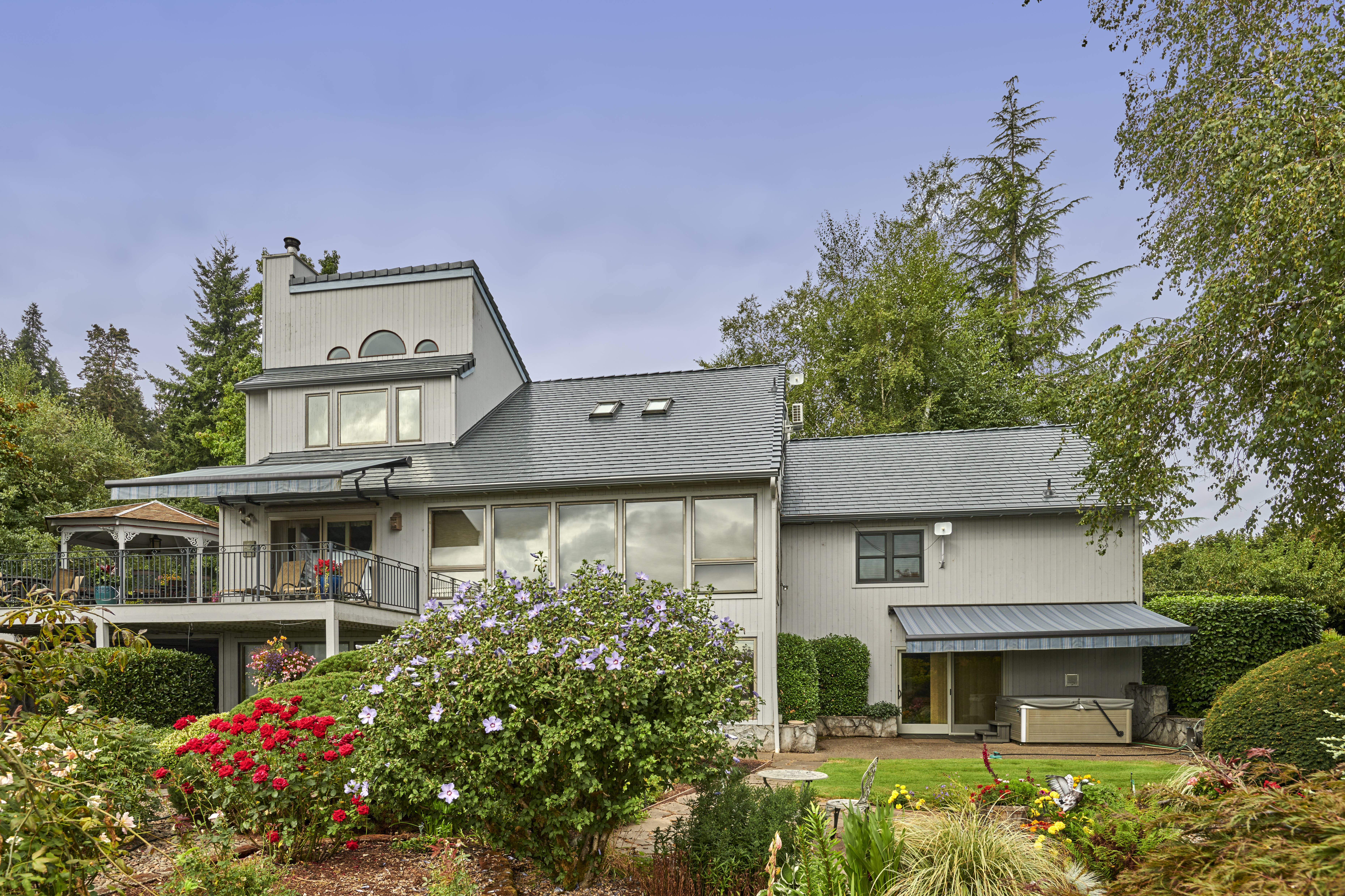 Rear elevation of a multi-story modern home in Amity, OR featuring Interlock deep charcoal aluminum slate roofing with complex multi-hip planes, skylights, and a top-floor dormer.
