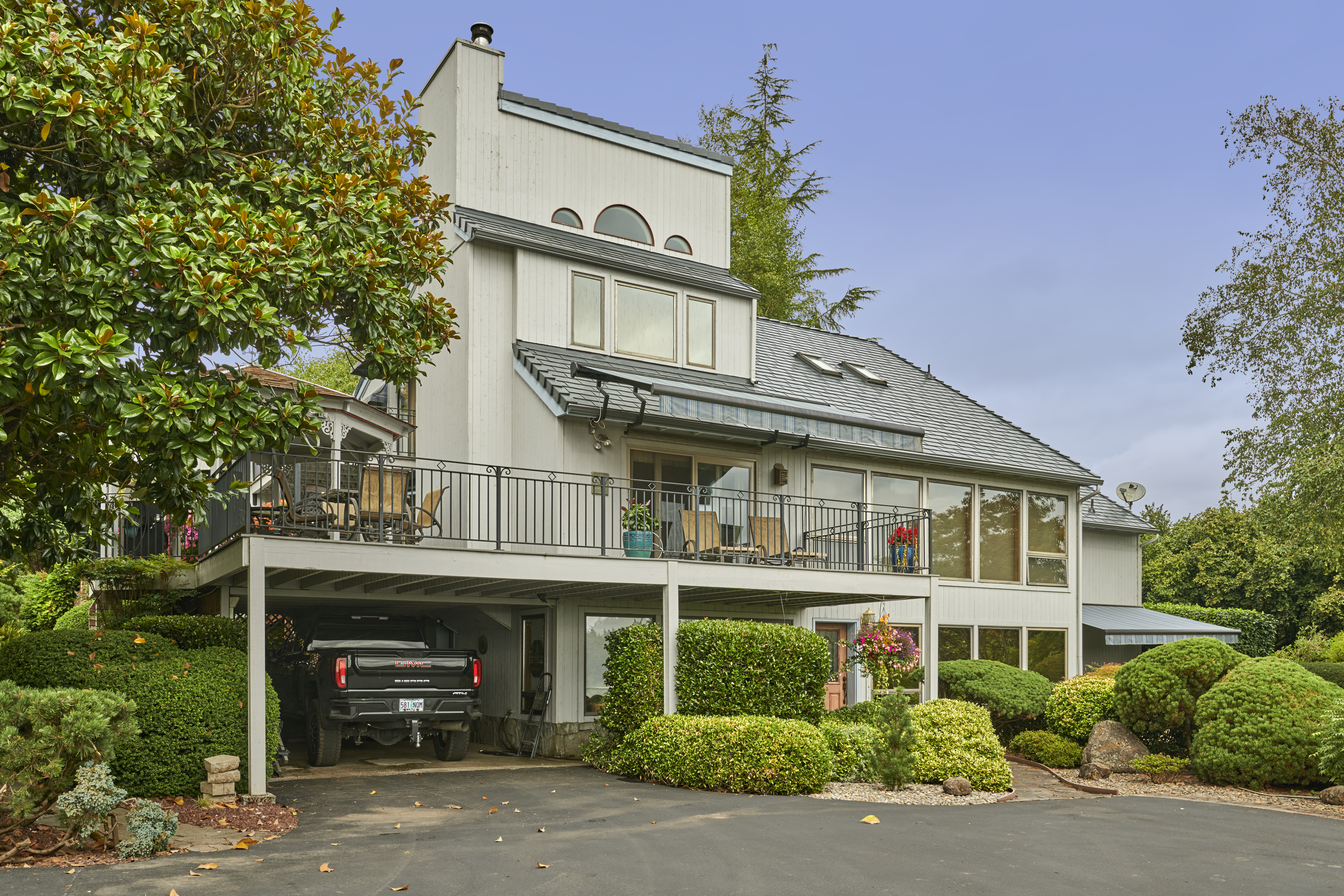 Multi-story home in Amity OR with deep charcoal Interlock aluminum slate roof, prominent chimney, skylights, and wraparound upper deck amid lush landscaping.