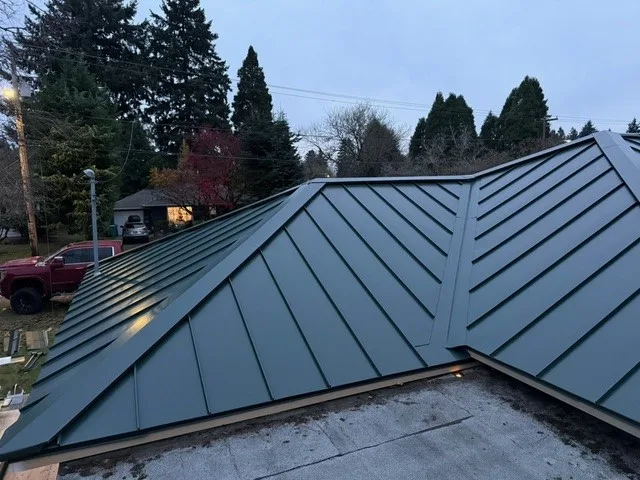 Aerial view of a complex hunter green standing seam aluminum roof with converging valleys on a single-family home in a forested Portland suburb.
