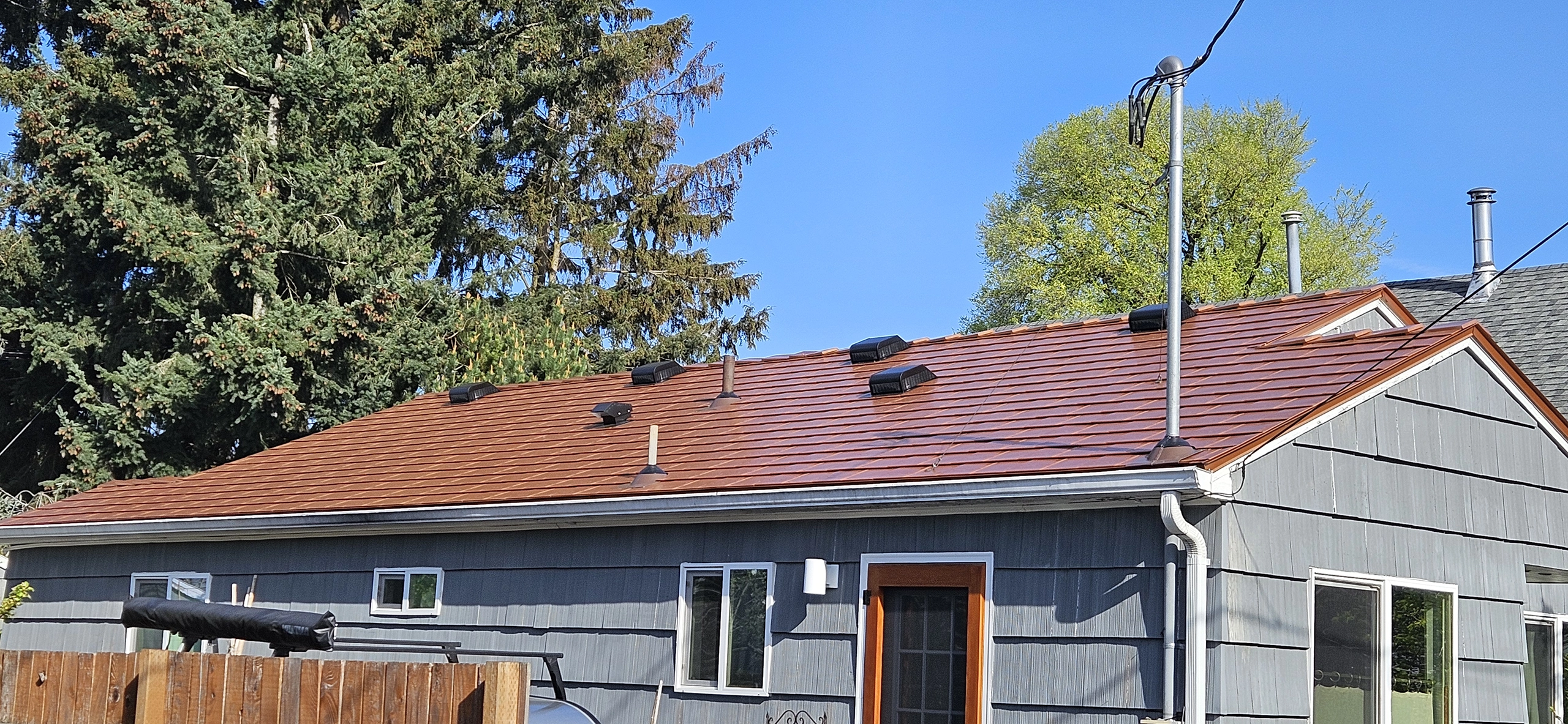 Single-story ranch home with Interlock aluminum slate roof in Copper Penny, featuring multiple roof louvers and vent pipes against a clear blue sky.