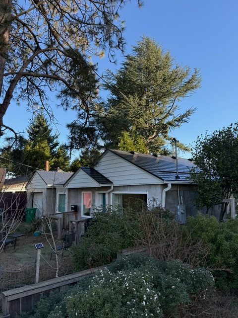 Single-story Ranch home with black Interlock aluminum slate metal roof and solar panels, set among mature trees in a suburban Portland neighborhood.