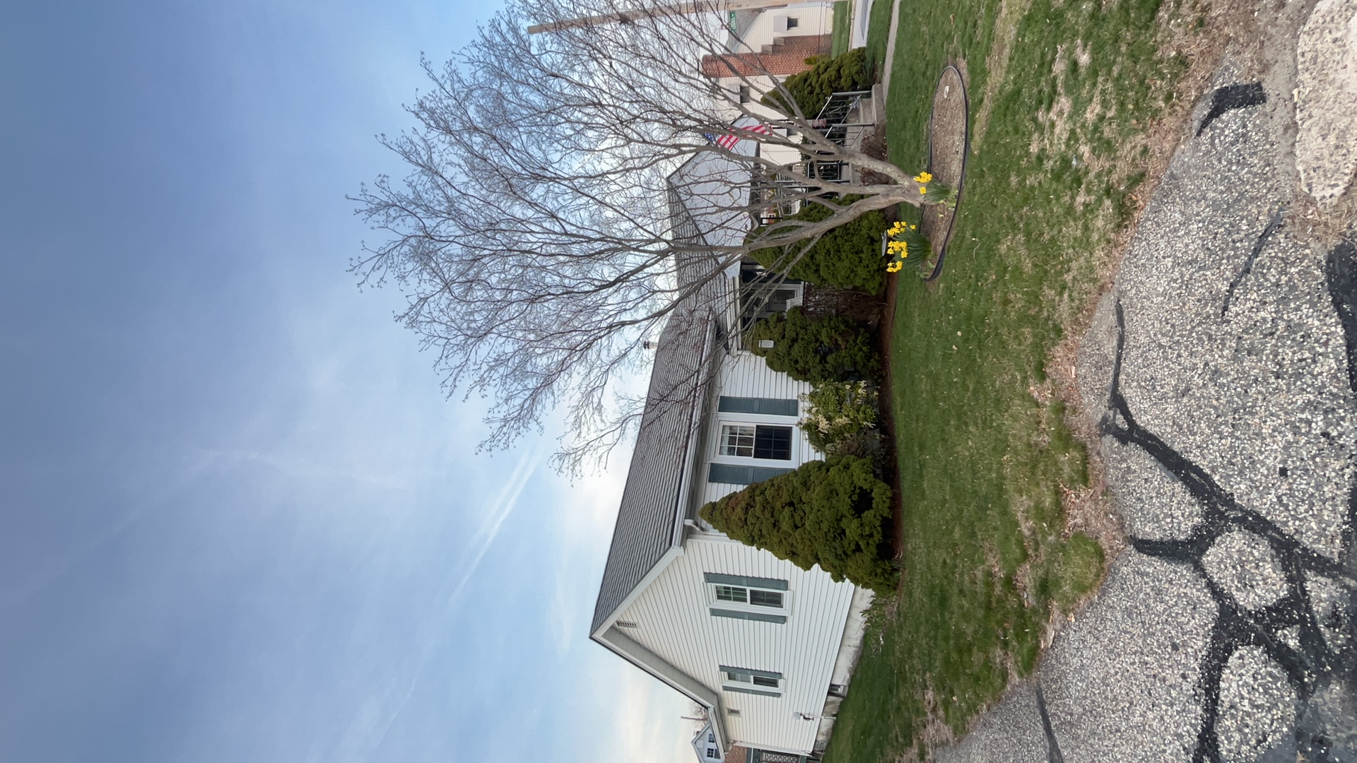 White ranch-style home in Pawtucket RI with Hunter Green Interlock aluminum shingle roof, green shutters, evergreen shrubs, and blooming daffodils.
