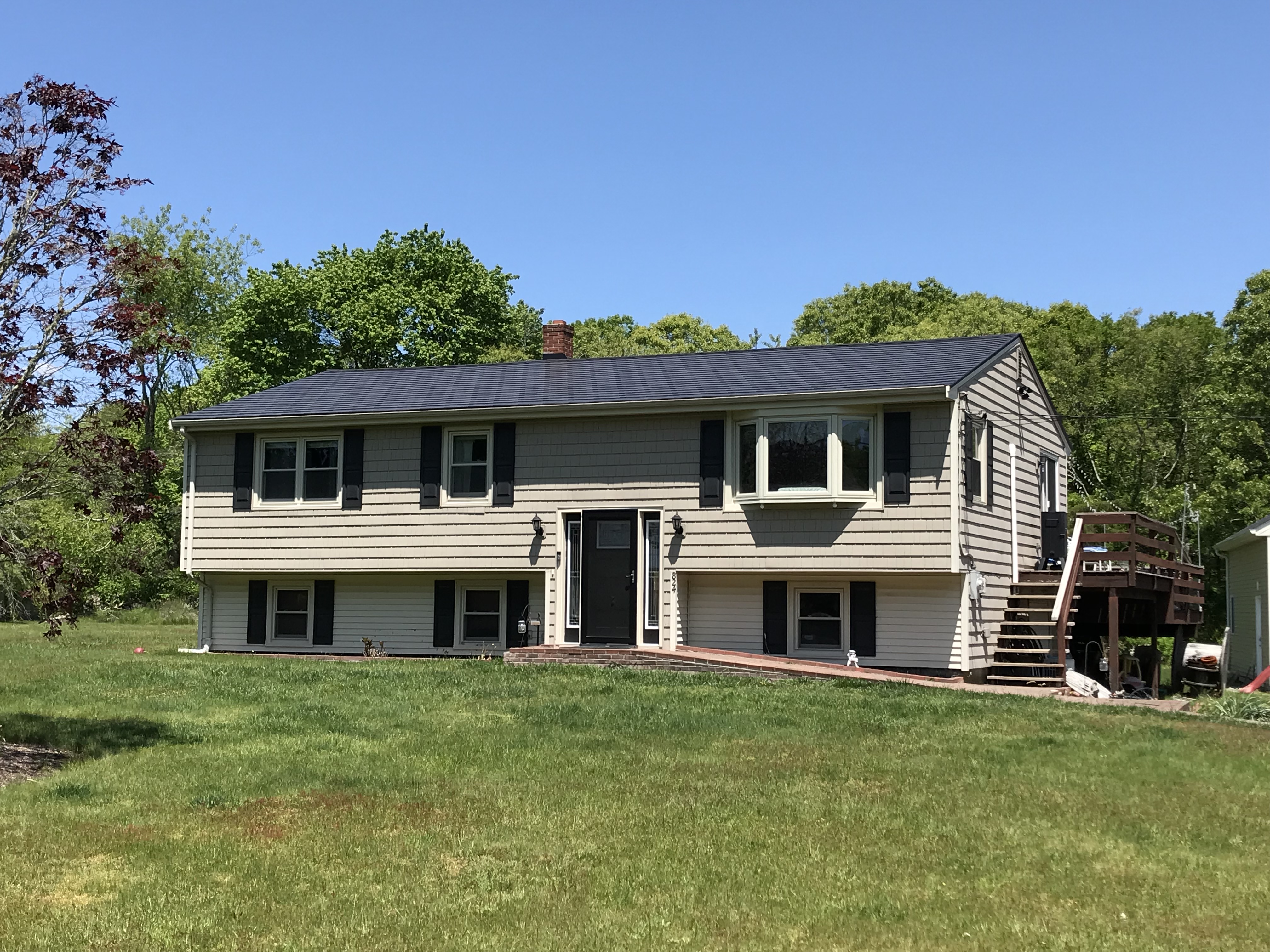 Two-story Colonial home in Tiverton RI with a dark charcoal Interlock aluminum slate metal roof, black shutters, and attached rear deck.