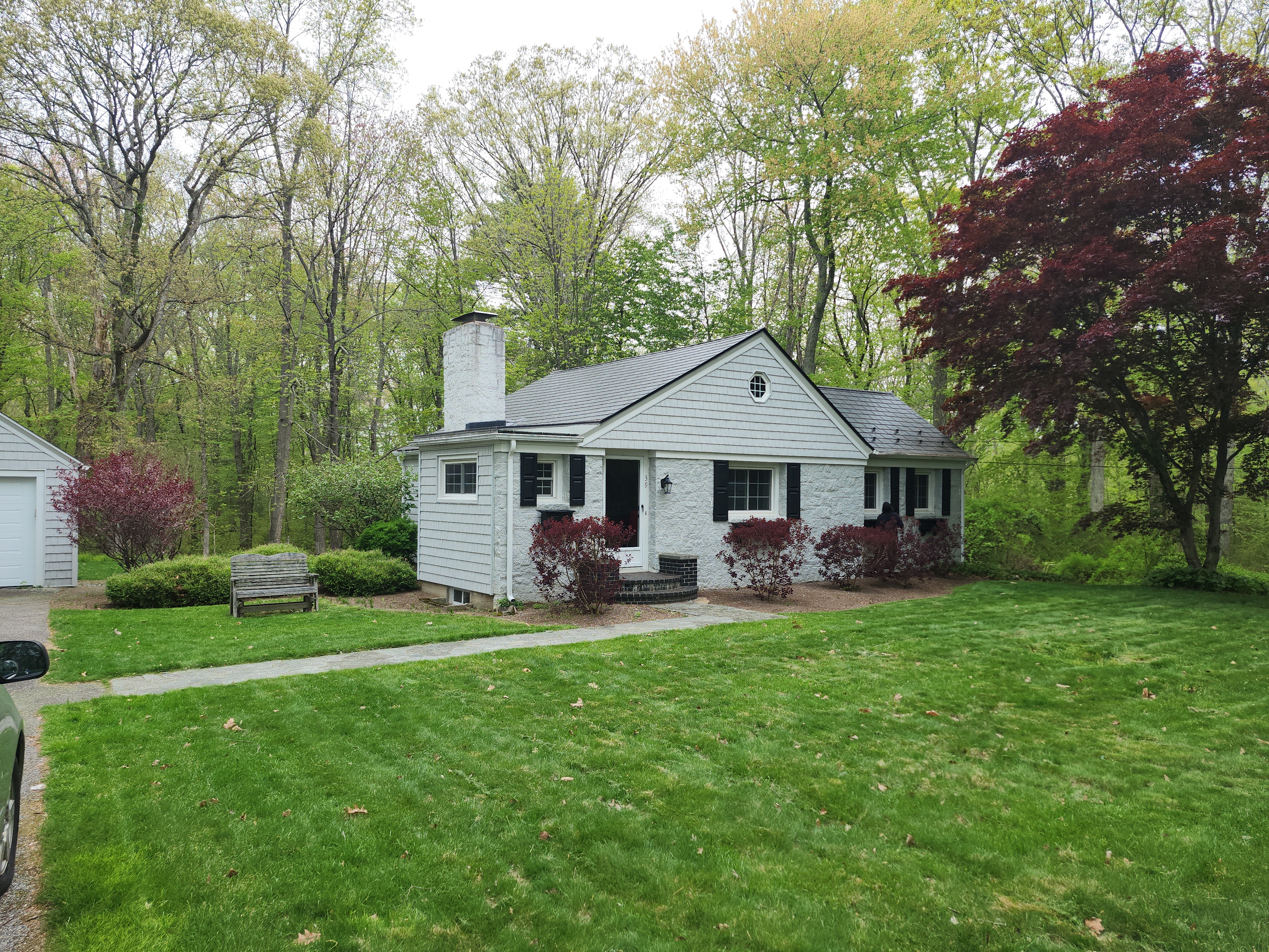 Cape Cod home in Gloucester RI with black Interlock aluminum slate metal roof, white painted stone exterior, black shutters, and tall painted chimney.