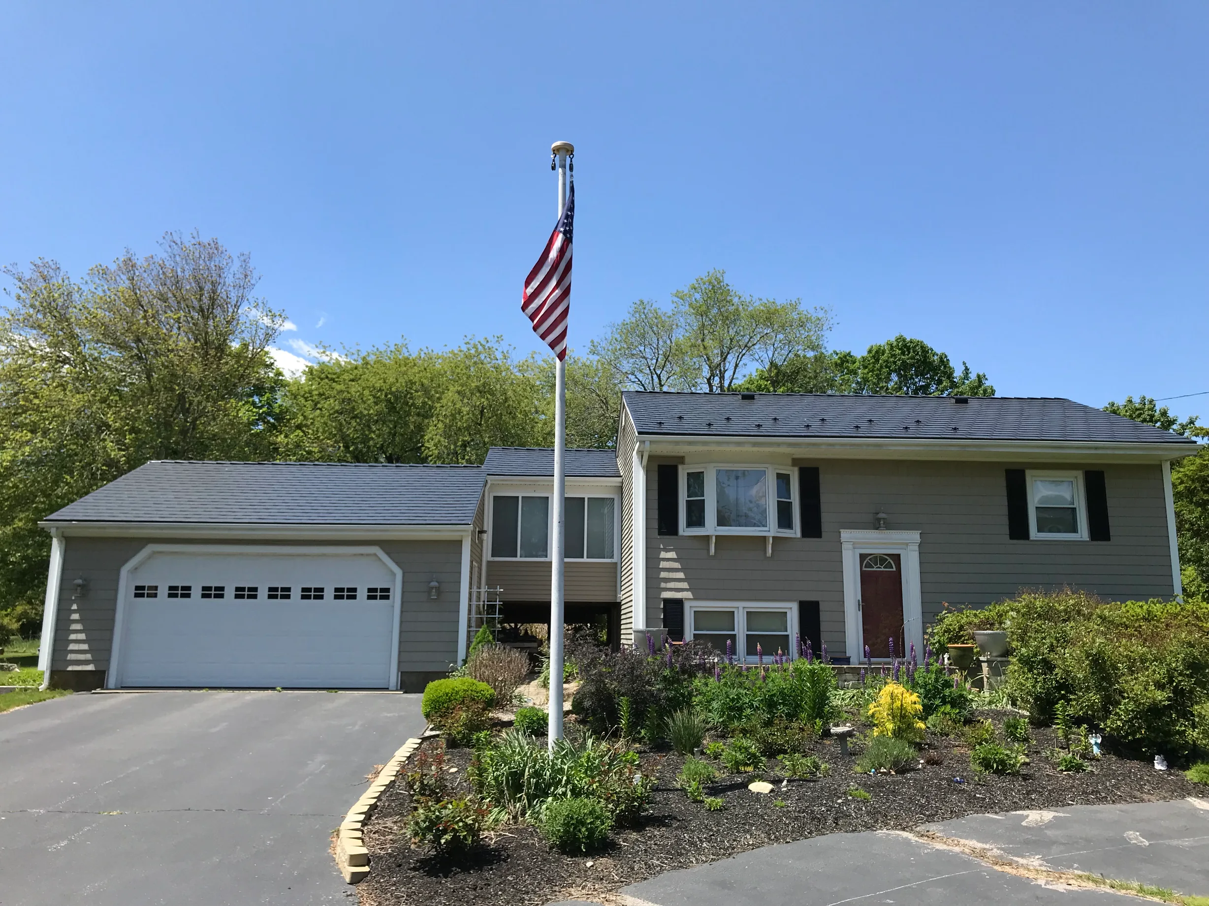 Black Interlock Slate aluminum roof on a grey two-storey home with a metal roof among green trees, Tiverton, Rhode Island