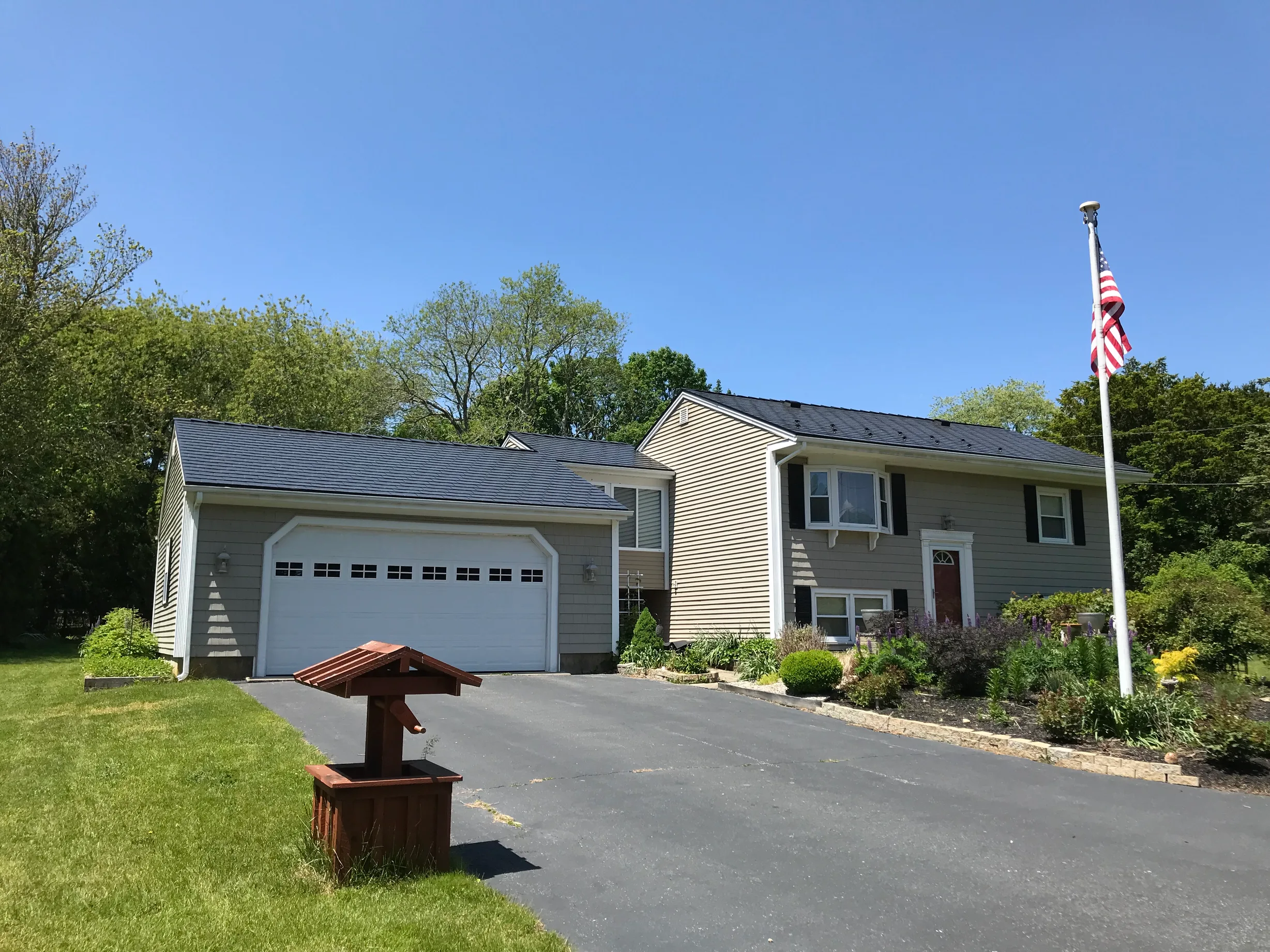 Black Interlock Slate aluminum roof on a beige ranch home with a metal roof in a lush green, Tiverton, Rhode Island