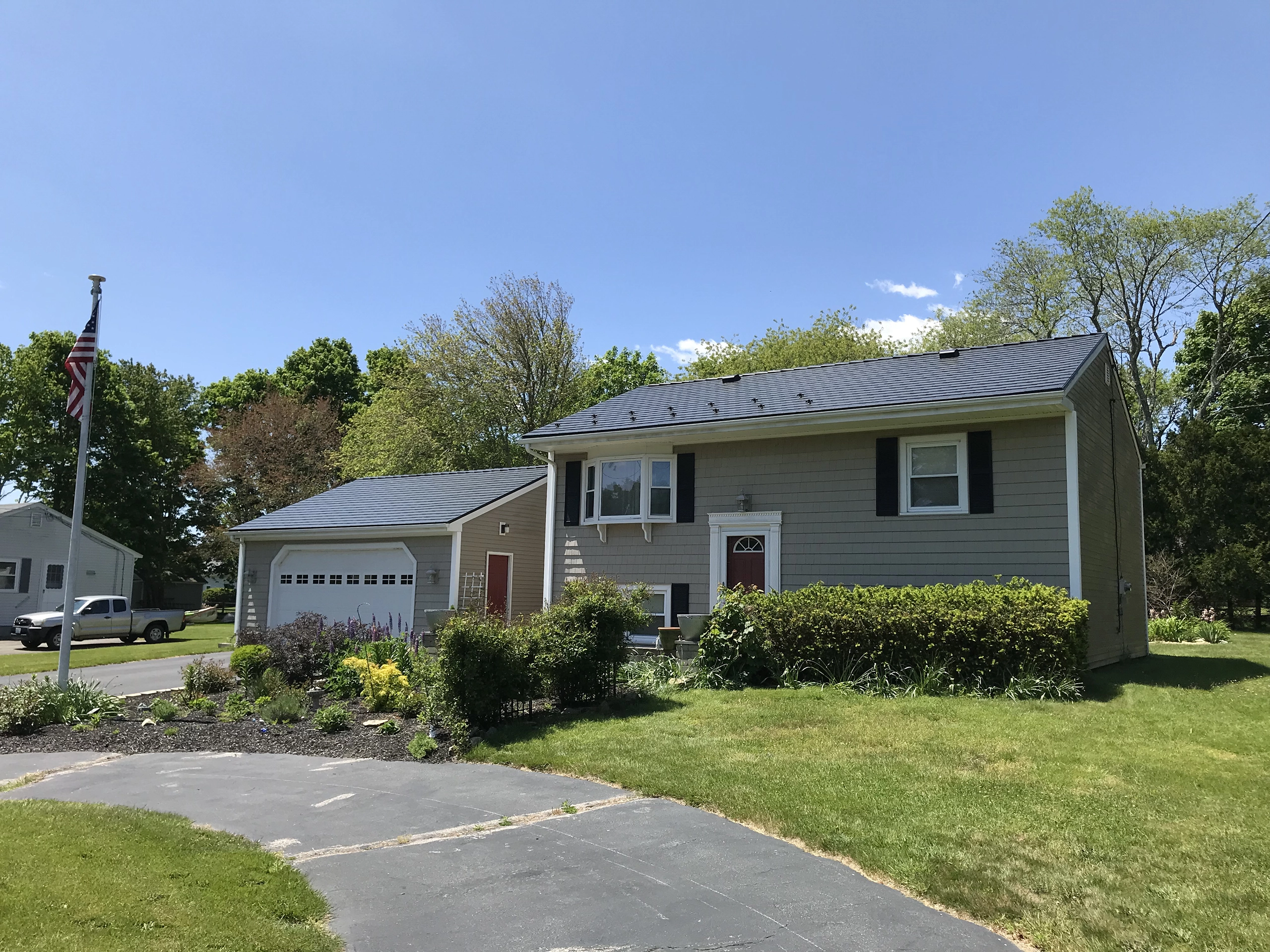 Two-story Colonial home in Tiverton, RI with a dark charcoal Interlock aluminum slate metal roof, gray vinyl siding, and manicured front landscaping.