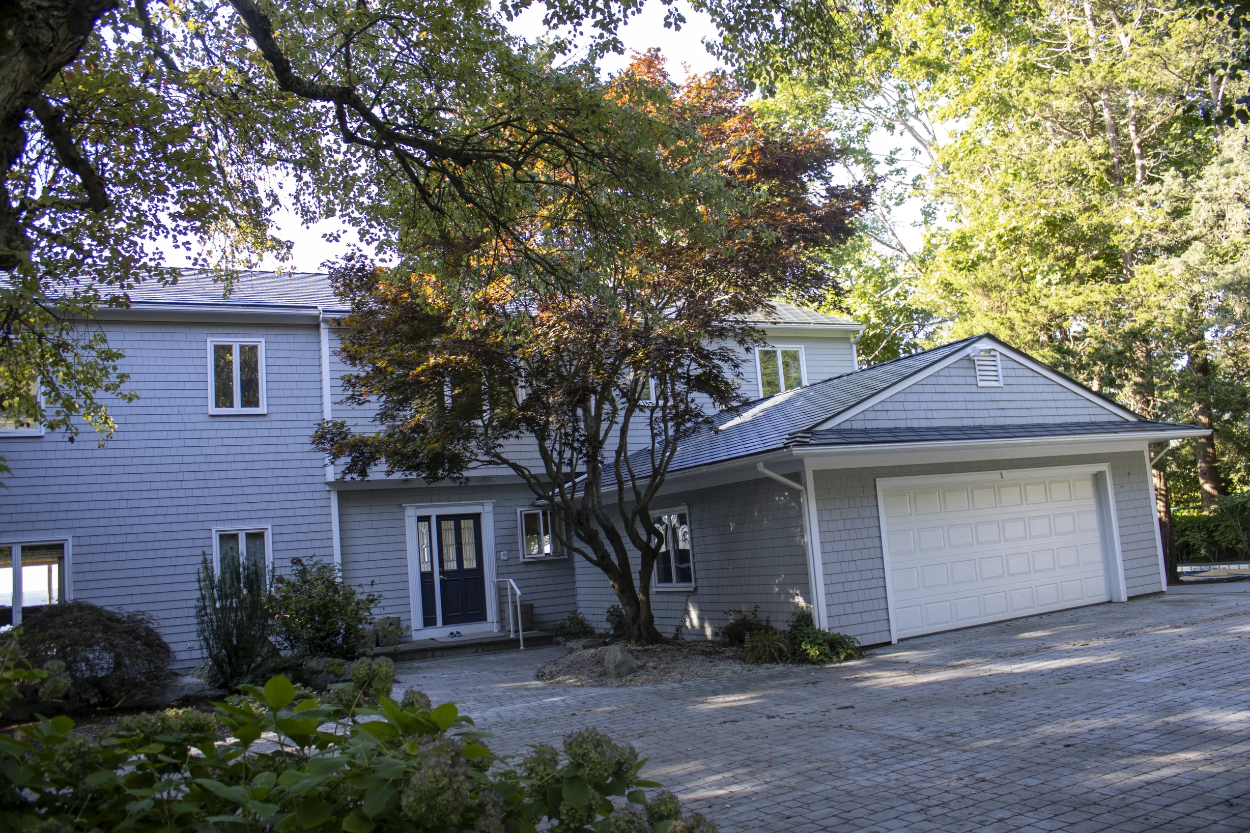Deep Charcoal Interlock Slate aluminum roof on a grey two-storey home with dormers among tall pines, Warwick, Rhode Island