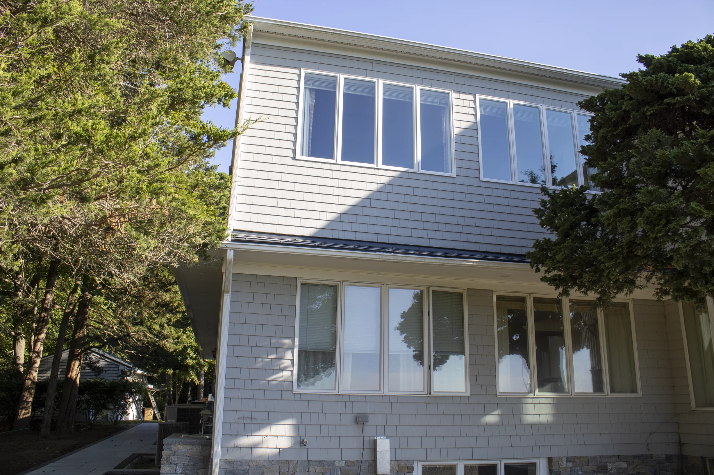 Deep Charcoal Interlock Slate aluminum roof on a grey Modern home with a metal roof among tall trees, Warwick, Rhode Island