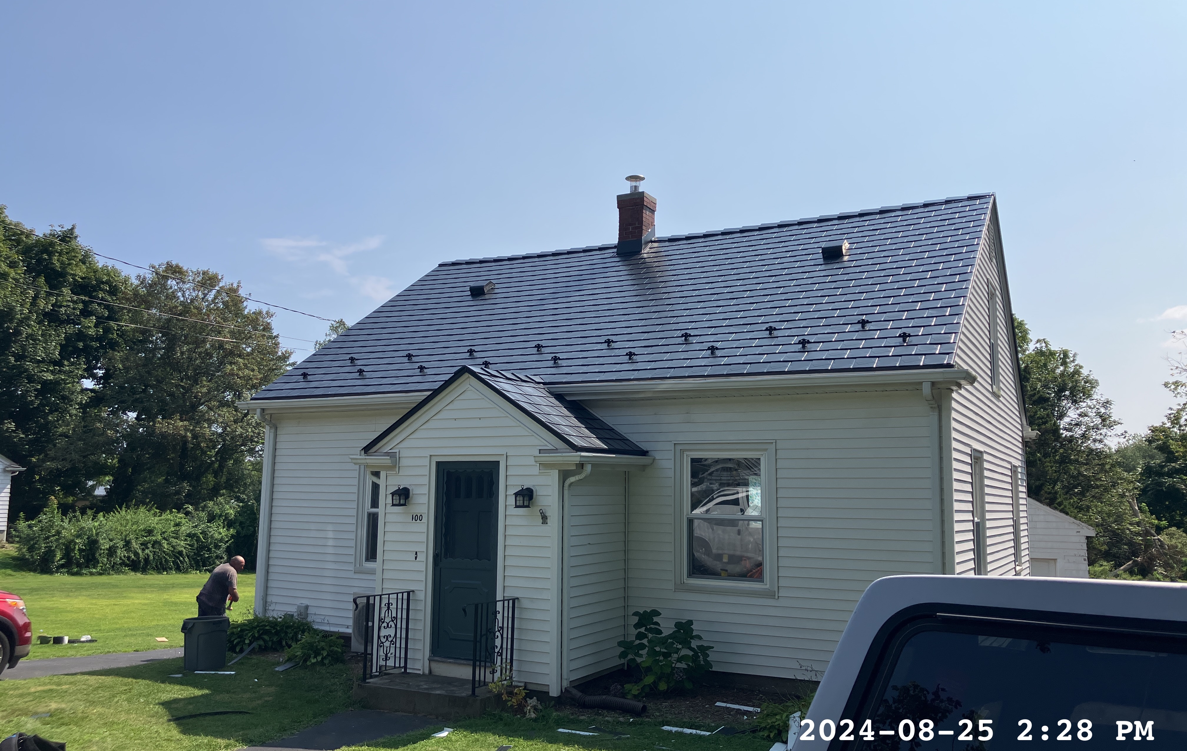 Cape Cod home with newly installed Interlock black aluminum slate metal roof, featuring a steep gable pitch, brick chimney, and small entry portico in Portsmouth, RI.