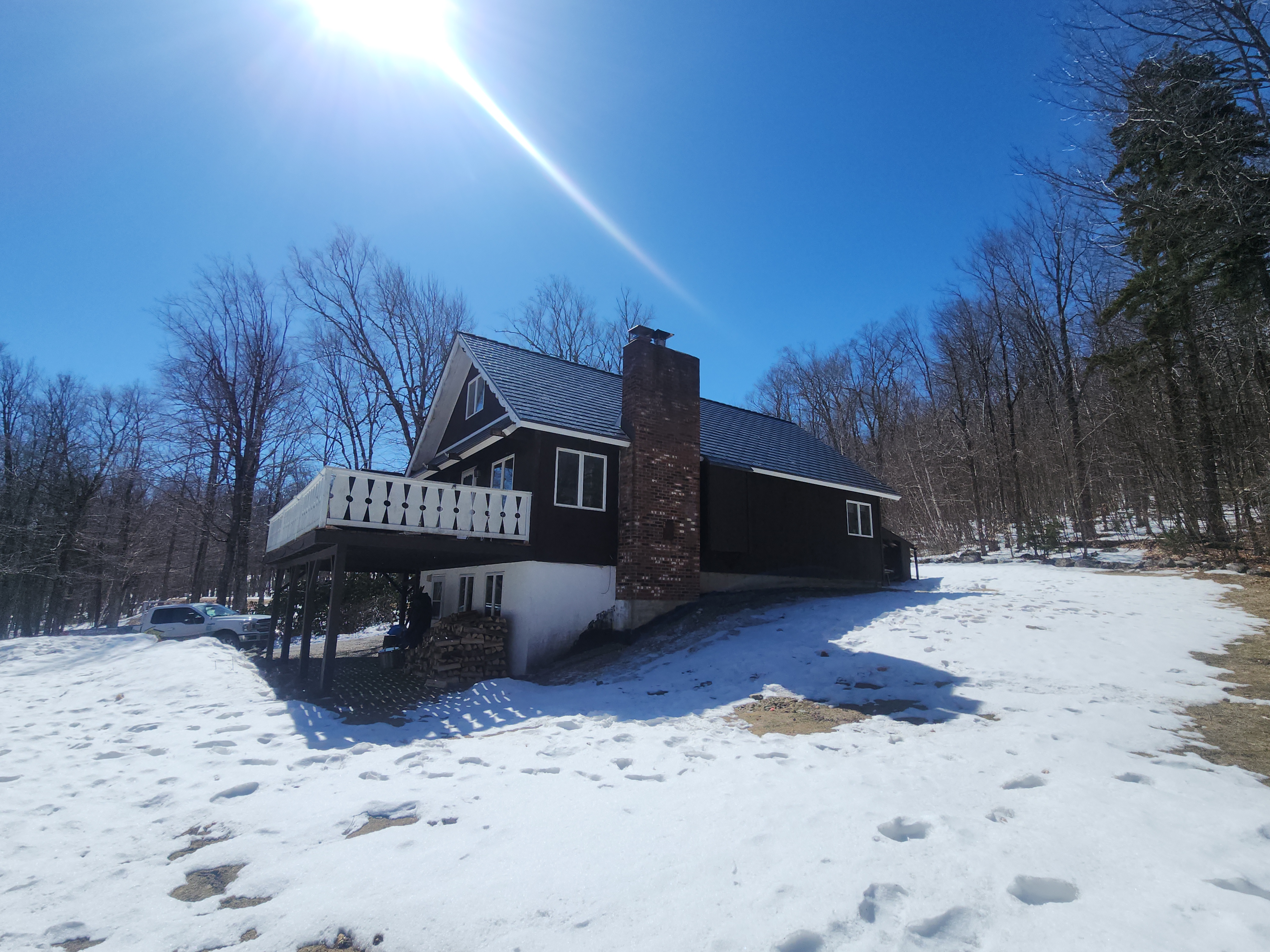Musket Grey Interlock cedar shingle metal roof on a dark-brown chalet-style Vermont home with brick chimney and elevated deck, surrounded by snow and bare trees.
