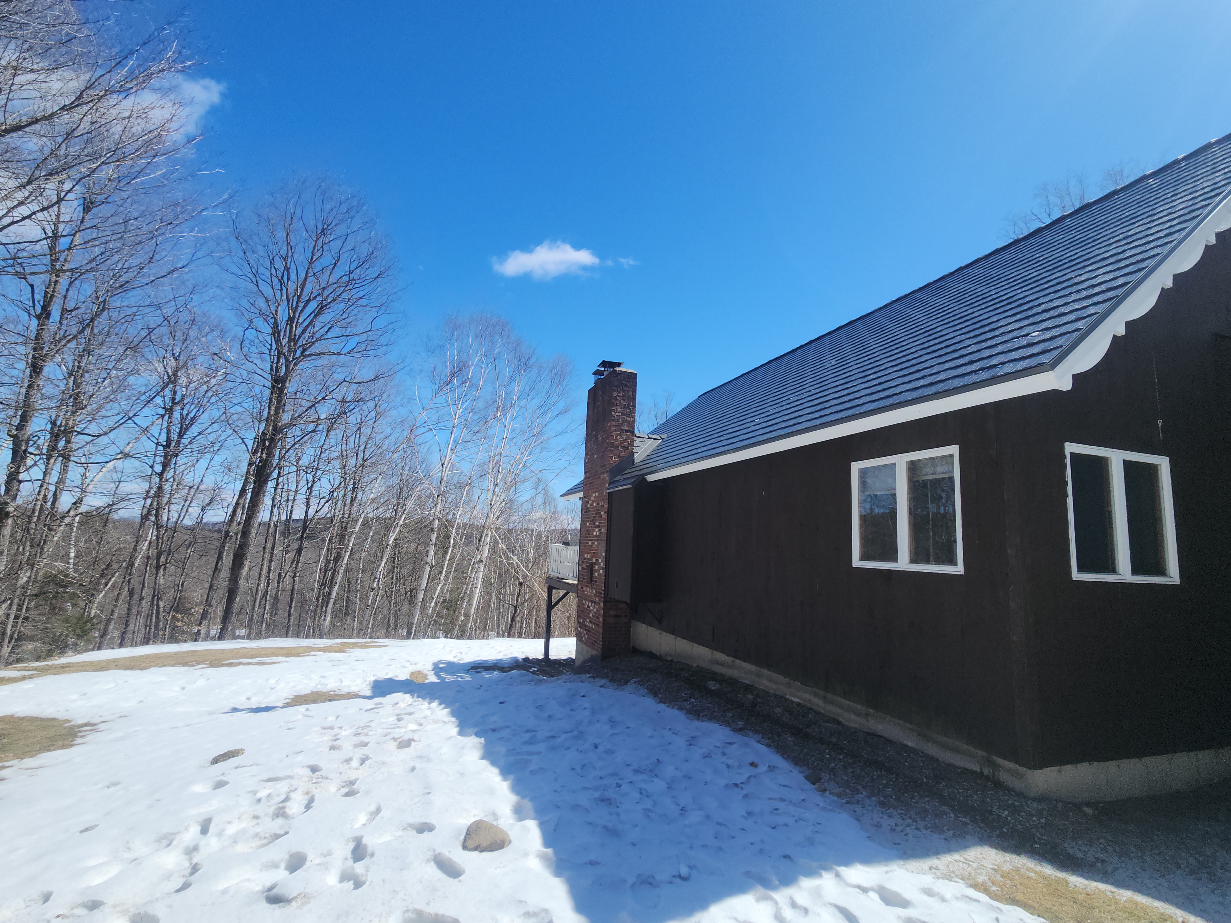 Musket Grey Interlock cedar shingle metal roof on a dark-brown ranch home in Vermont, featuring a brick chimney, surrounded by bare winter trees.