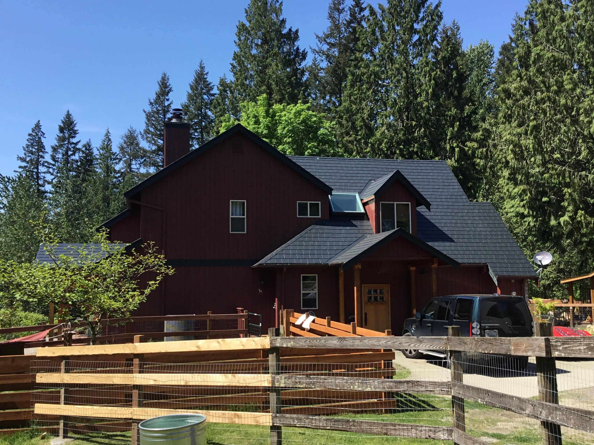 Charcoal Grey Interlock Shingle aluminum roof on a red two-storey home with dormers in a forested rural, Woodinville, Washington