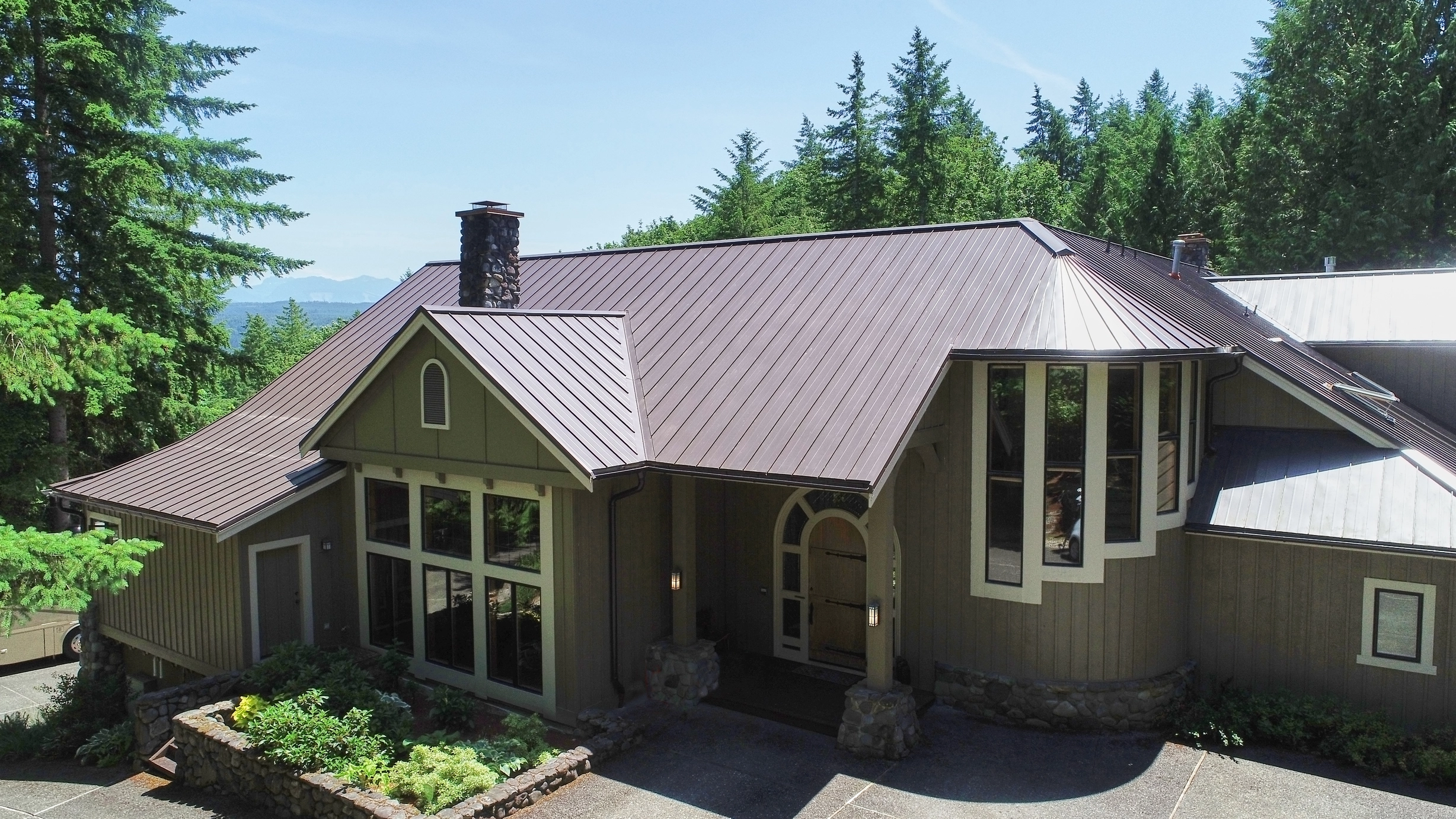 Tudor Brown Interlock Standing Seam aluminum roof on a brown two-storey home with dormers among tall pines, Fall City, Washington