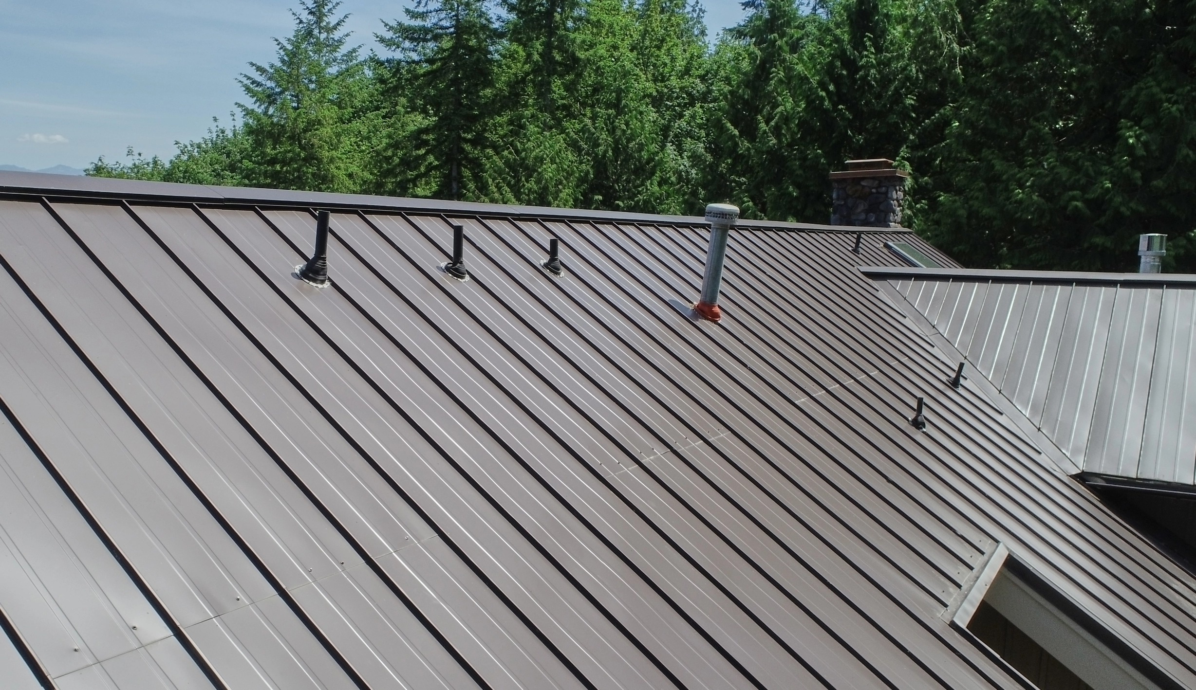 Tudor Brown Interlock Standing Seam aluminum roof on a brown single-storey Tudor home with dormers among tall, Fall City, Washington