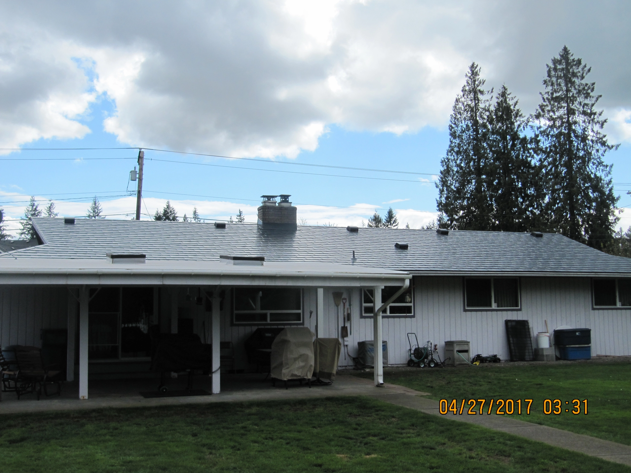 Deep Charcoal Interlock Slate aluminum roof on a white ranch home with a metal roof among tall evergreen, Marysville, Washington
