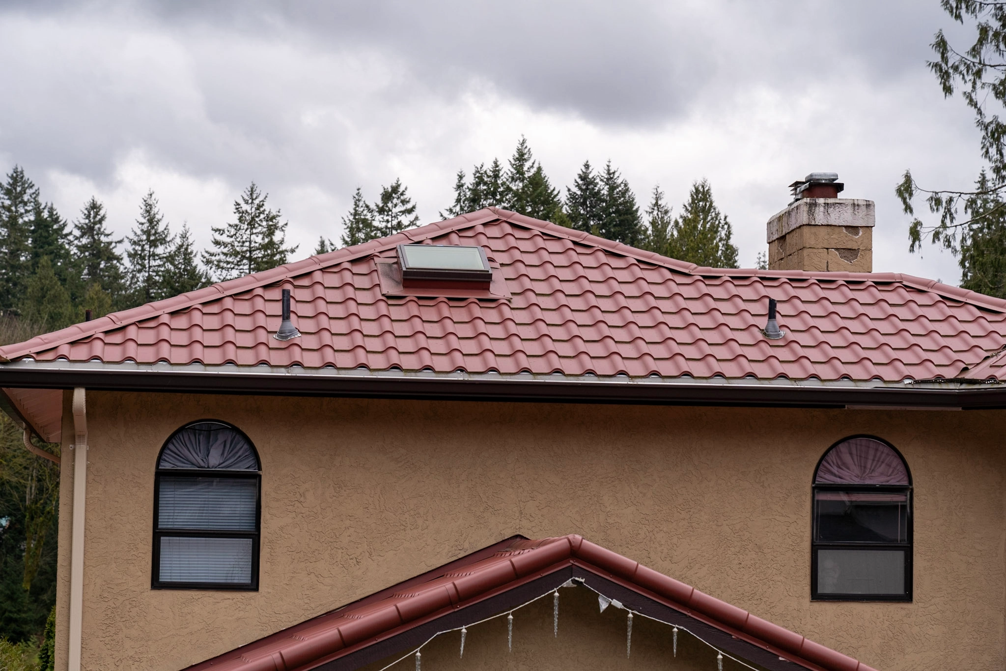 Tile Red Interlock Tile aluminum roof on a tan house with red tile roof and red trim in a forested, Woodinville, Washington