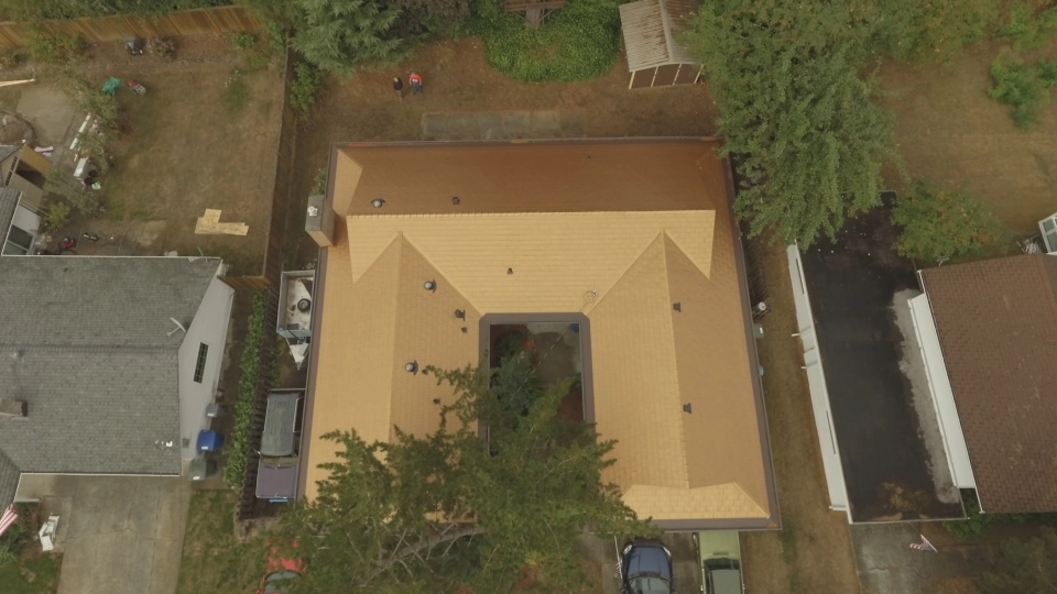 Aged Copper Interlock Cedar Shingle aluminum roof on a tan two-storey home with a metal roof among tall trees, Bellevue, Washington