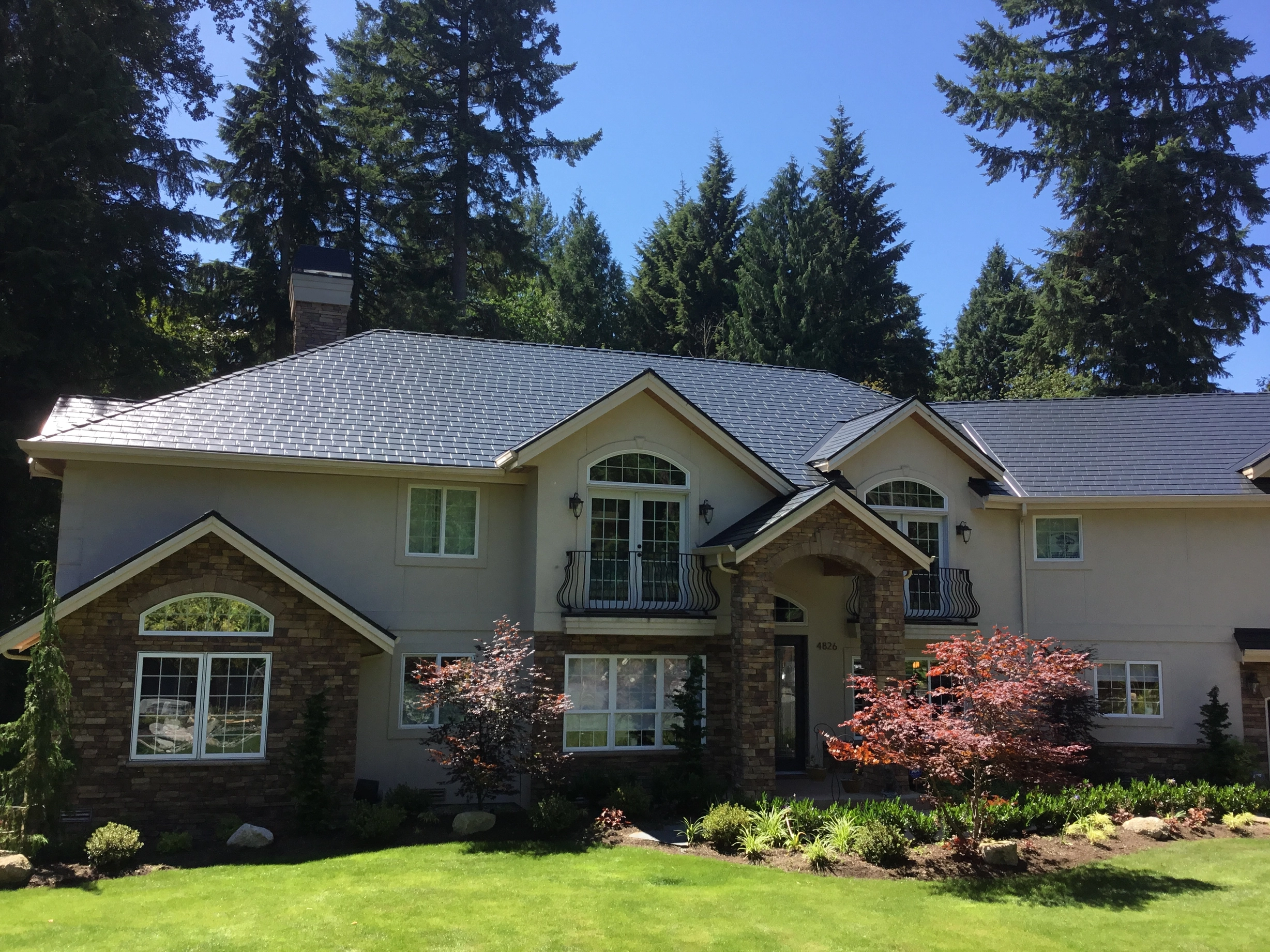 Black Interlock Slate aluminum roof on a beige two-storey home with dormers among tall pines, Bothell, Washington