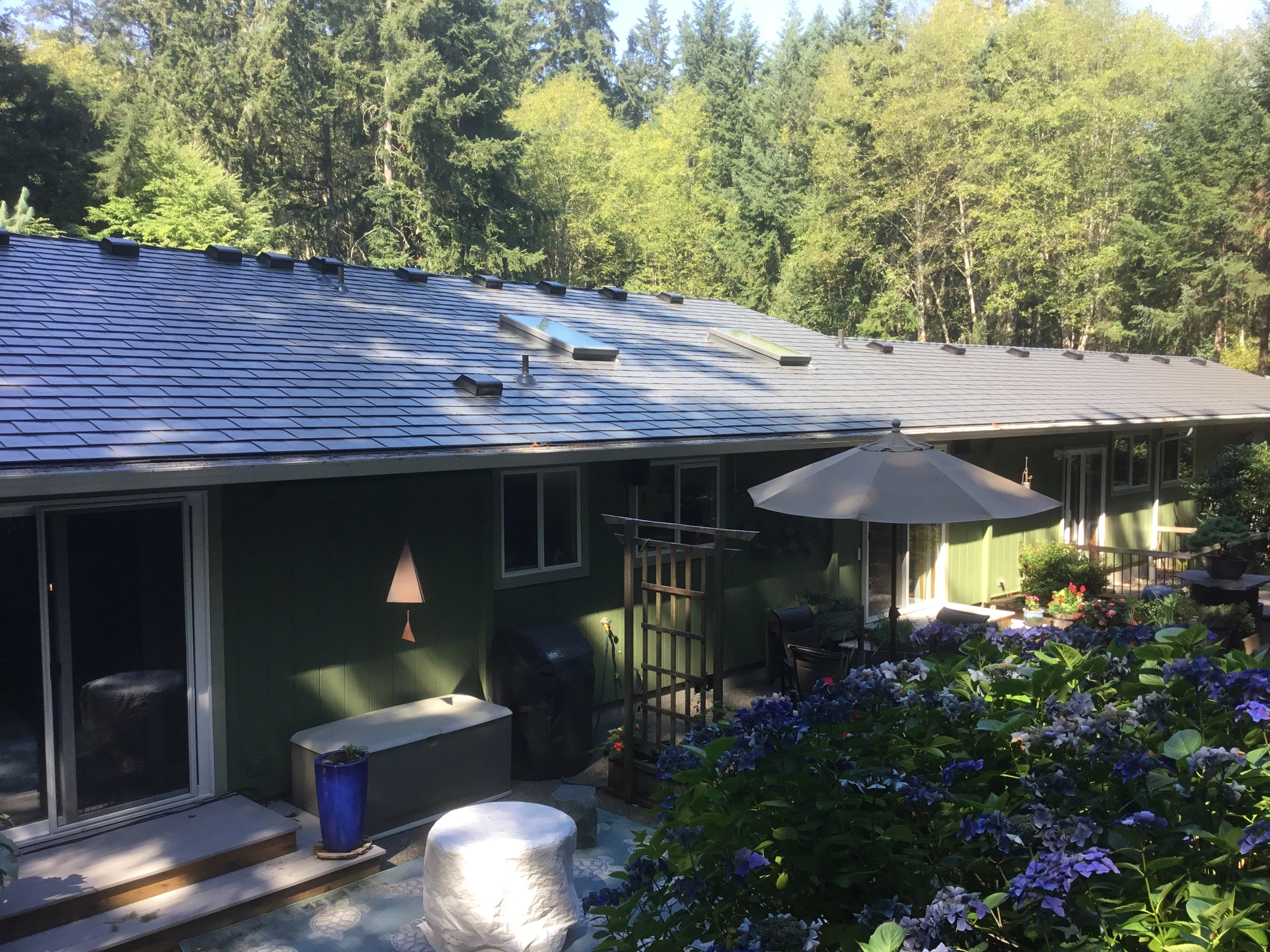 Deep Charcoal Interlock Slate aluminum roof on a two-storey green home with a metal roof in a forested area, Poulsbo, Washington
