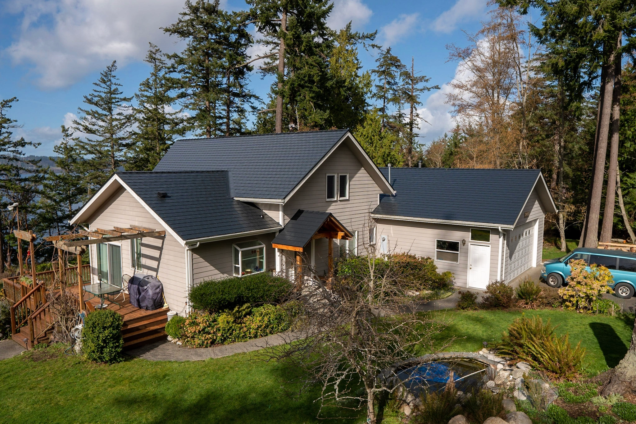 Black Interlock Slate aluminum roof on a grey two-storey home with dormers among tall trees, Langley, Washington