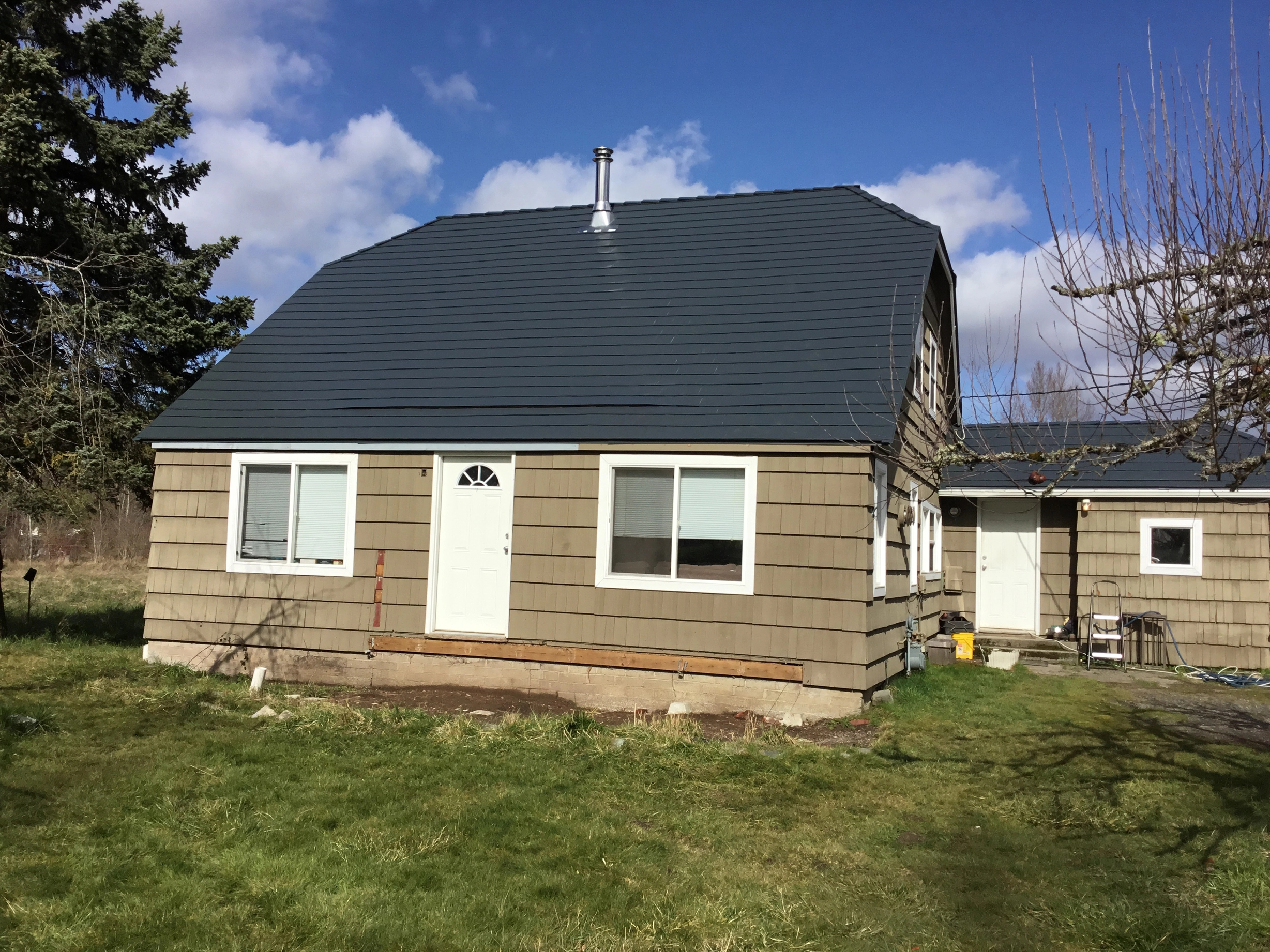 Deep Charcoal Interlock Slate aluminum roof on a tan single-family home with a metal roof in a forested, Tacoma, Washington