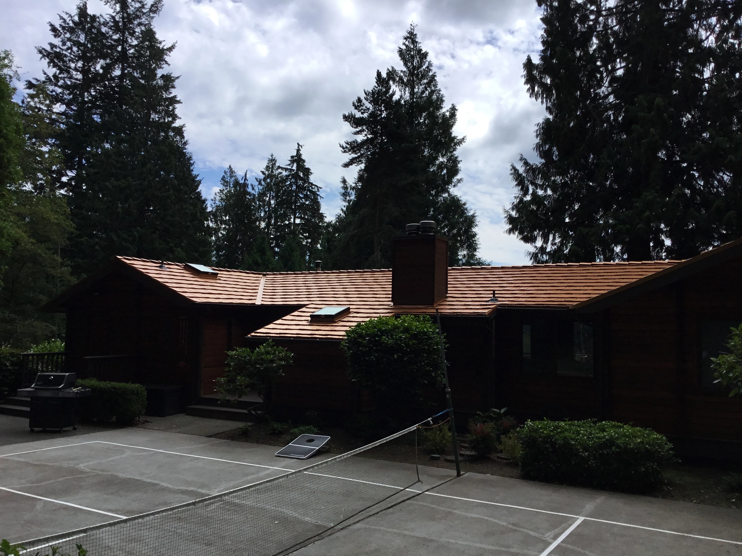 Copper Penny Interlock Shake aluminum roof on a dark red ranch-style home with chimney among tall, Bainbridge Island, Washington
