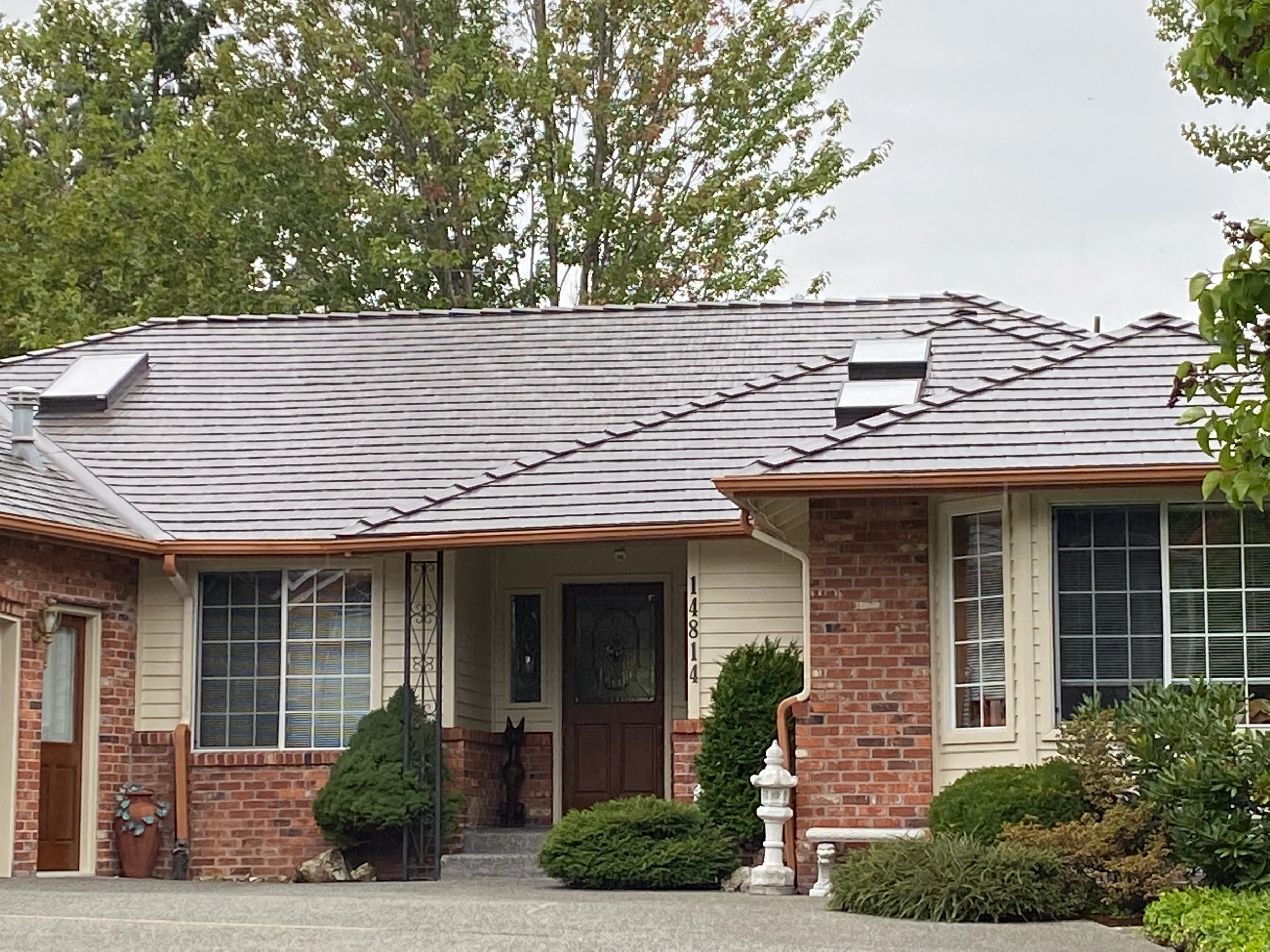 Tudor Brown Interlock Cedar Shingle aluminum roof on a Tudor home with brick and cream siding among forested, Mill Creek, Washington