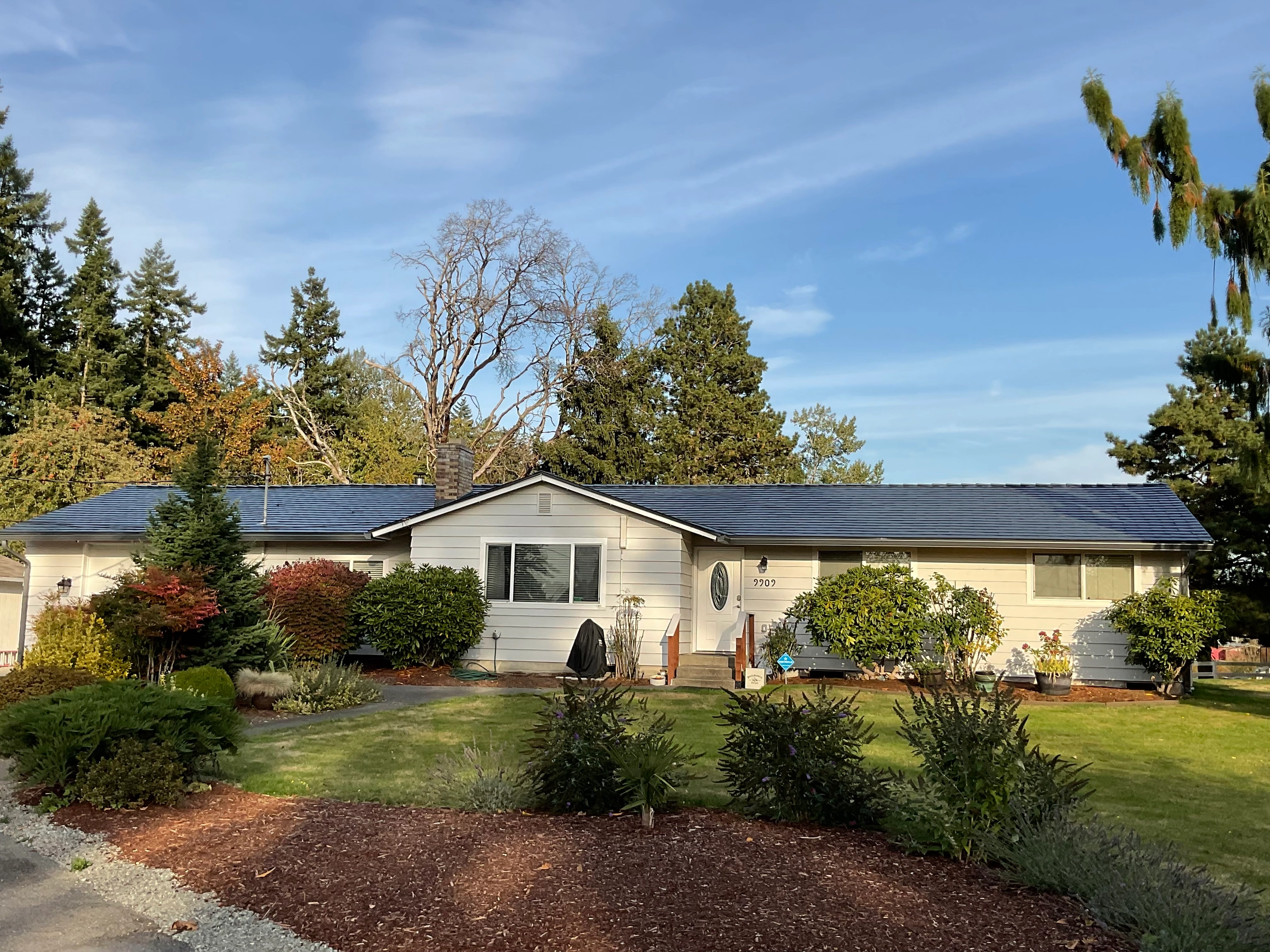Deep Charcoal Interlock Slate aluminum roof on a white ranch style home with a metal roof among tall trees, Tacoma, Washington