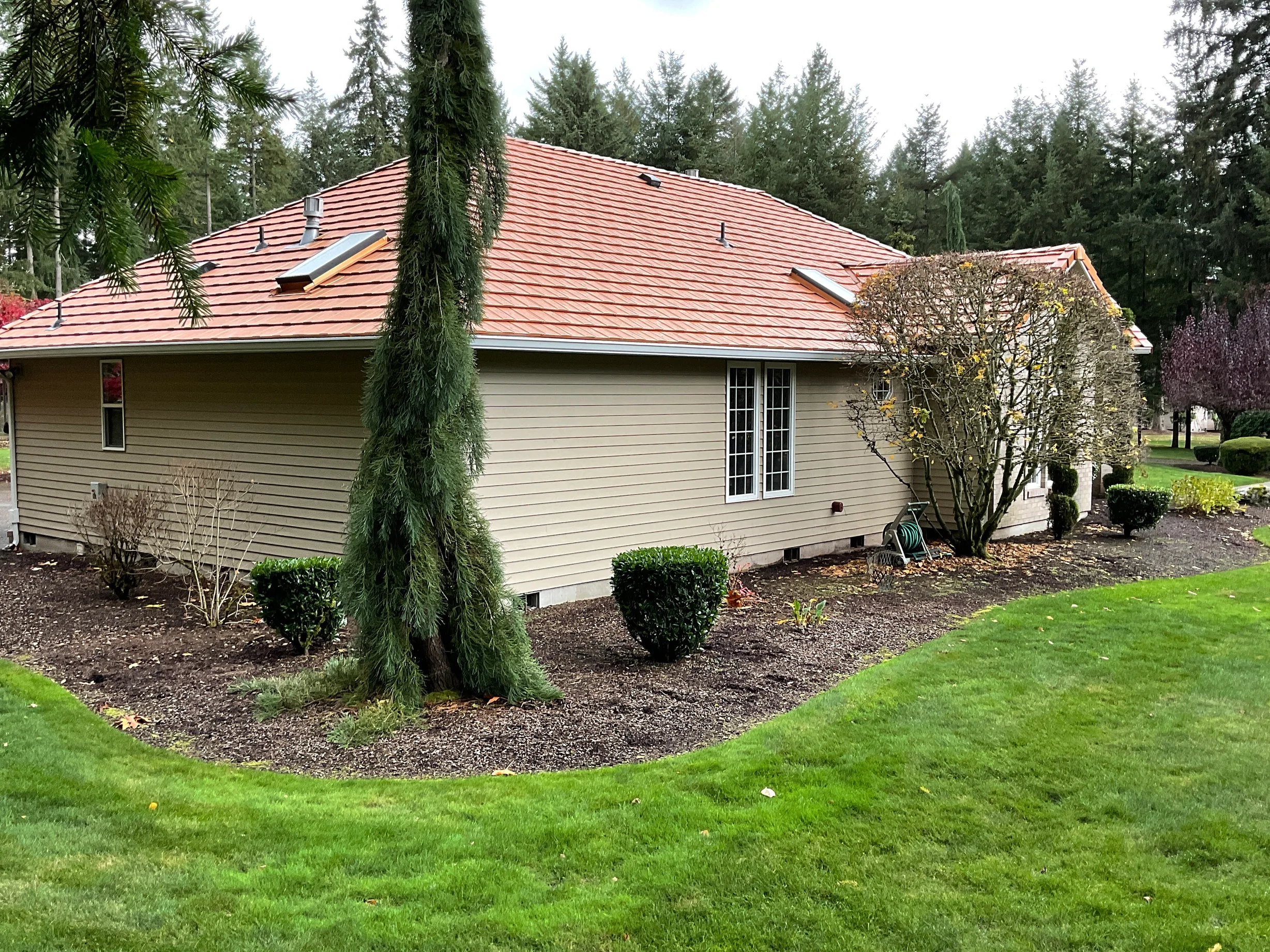 Copper Penny Interlock Shake aluminum roof on a beige ranch-style home with a red metal roof in a forest, Auburn, Washington